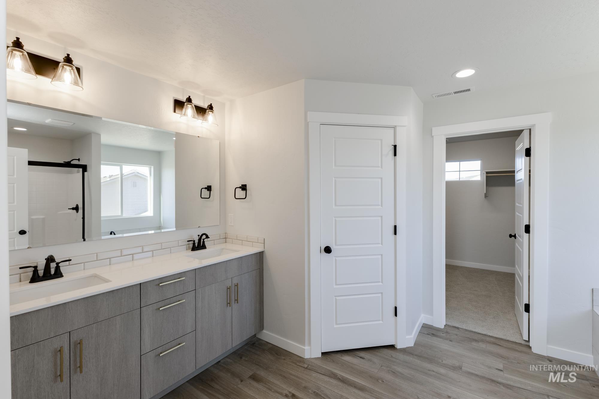 Full bath with recessed lighting, double vanity, a walk in closet, a shower stall, and light wood-style floors