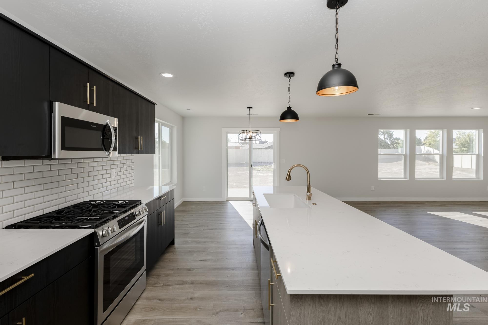 Kitchen with appliances with stainless steel finishes, dark cabinetry, hanging light fixtures, a kitchen island with sink, and light wood-type flooring