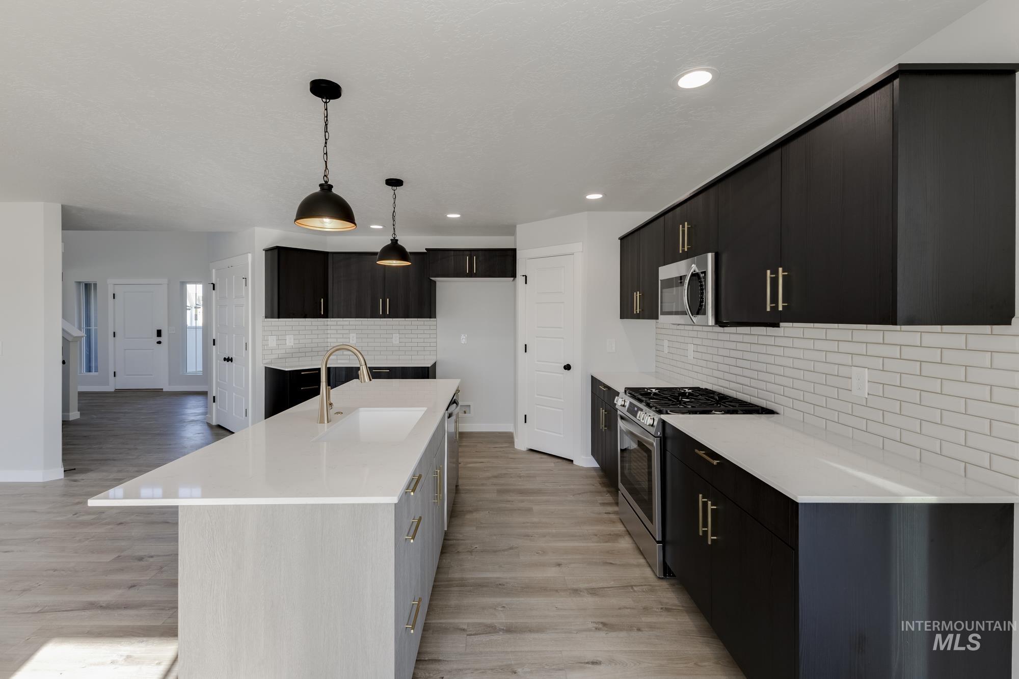 Kitchen featuring stainless steel appliances, pendant lighting, a kitchen island with sink, light wood-style floors, and light stone countertops