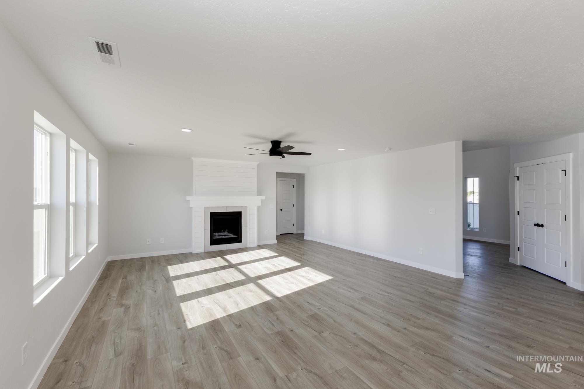 Unfurnished living room with healthy amount of natural light, a fireplace, light wood-type flooring, recessed lighting, and a ceiling fan