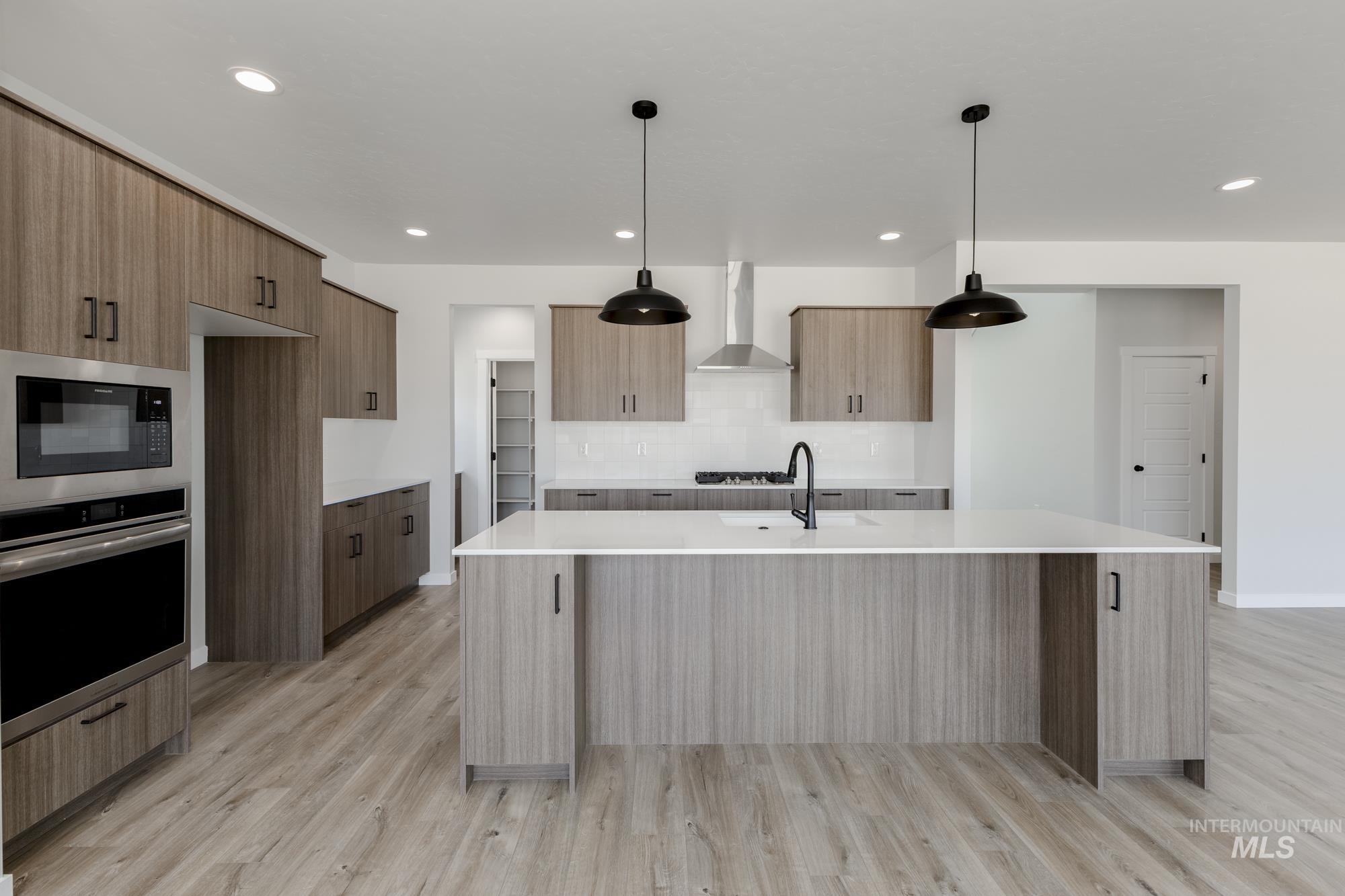 Kitchen with modern cabinets, stainless steel oven, decorative backsplash, light stone countertops, and hanging light fixtures