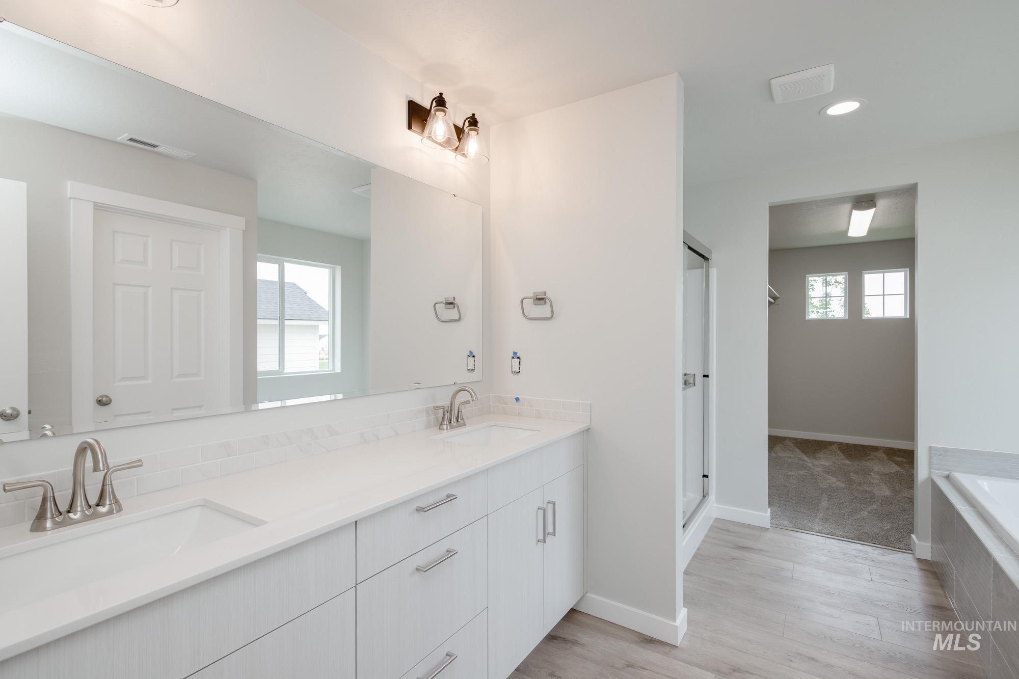 Full bath with a garden tub, healthy amount of natural light, double vanity, light wood-style floors, and recessed lighting