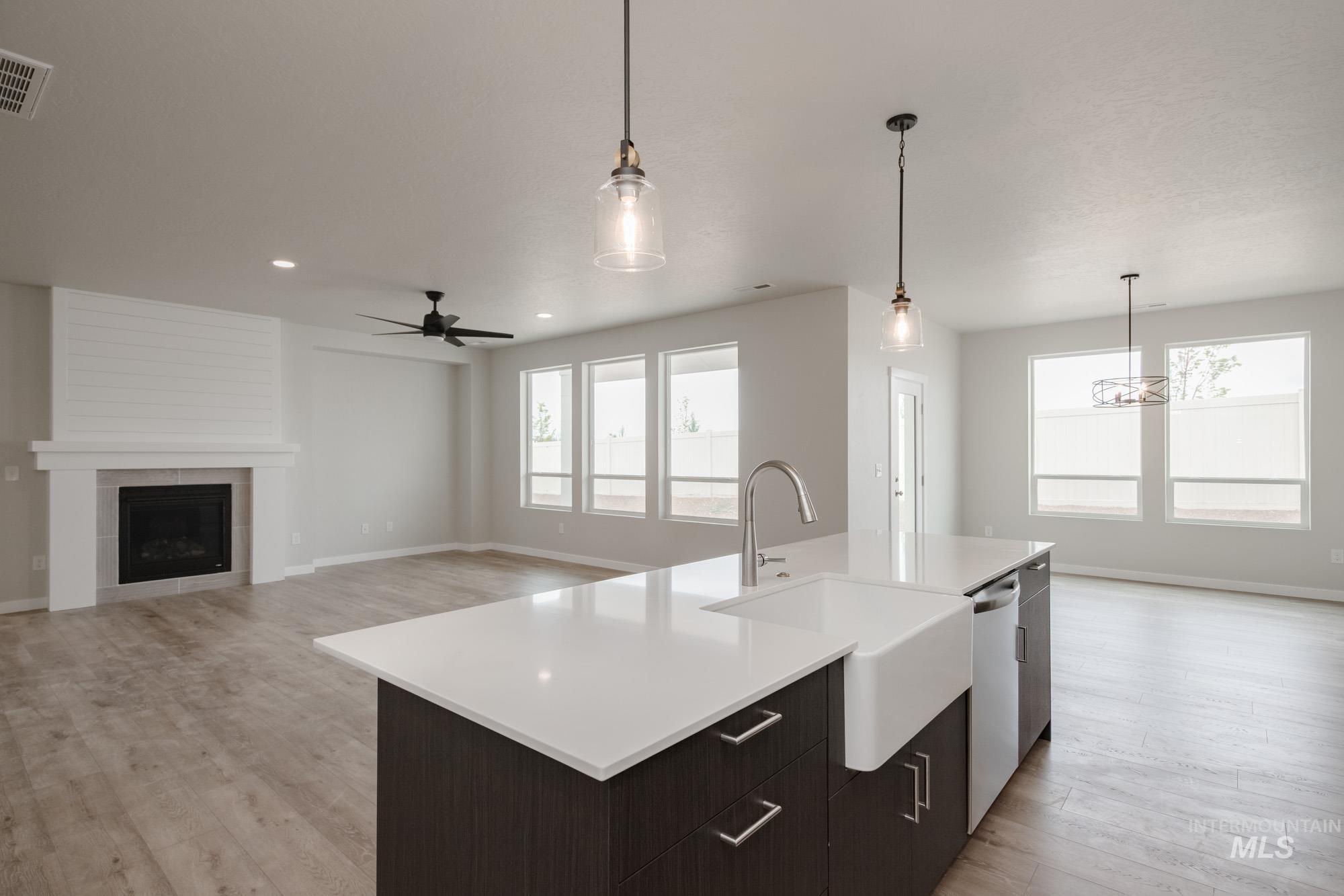 Kitchen featuring open floor plan, pendant lighting, an island with sink, a ceiling fan, and a tile fireplace