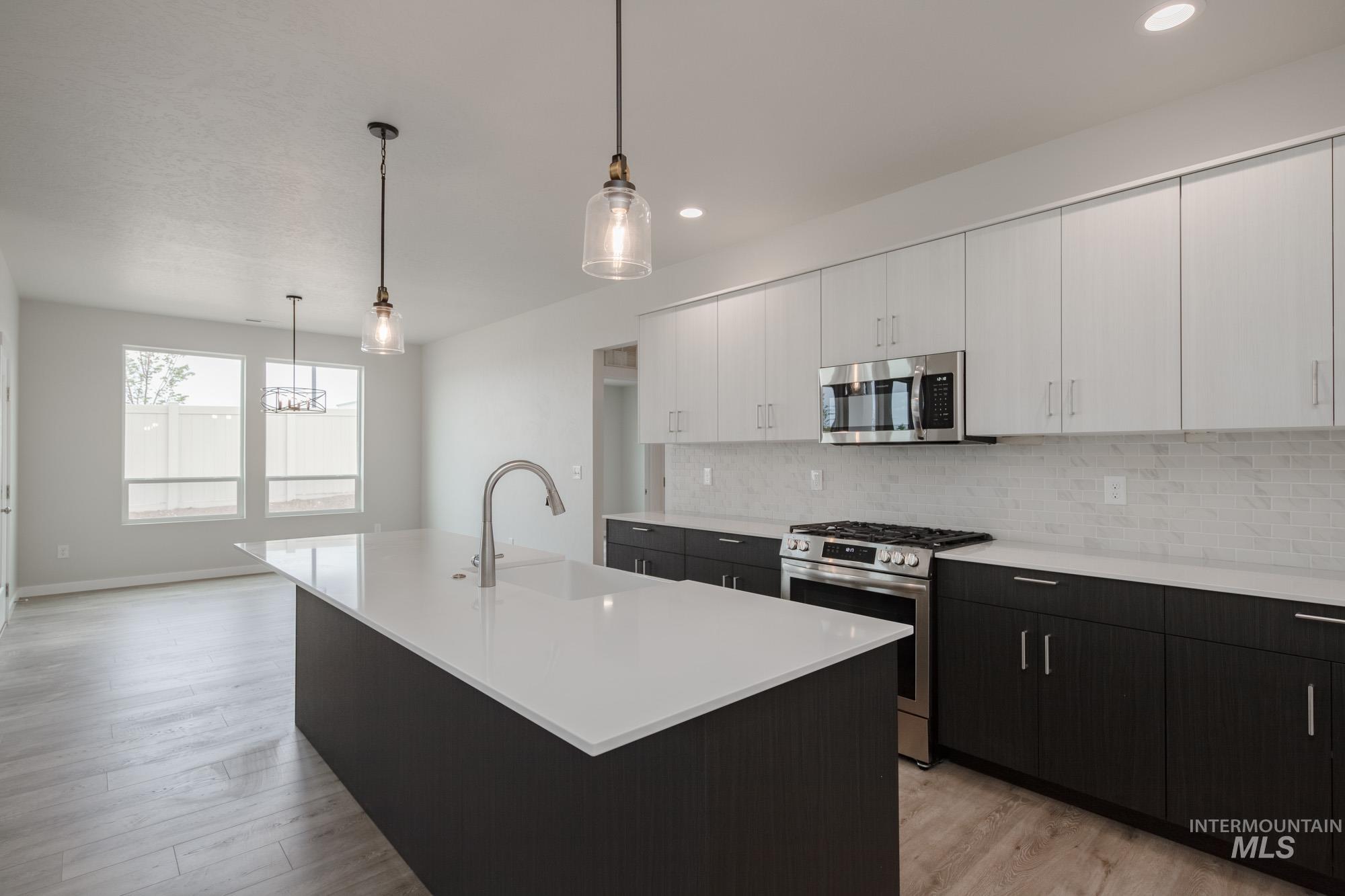 Kitchen featuring stainless steel appliances, dark cabinetry, tasteful backsplash, decorative light fixtures, and white cabinetry