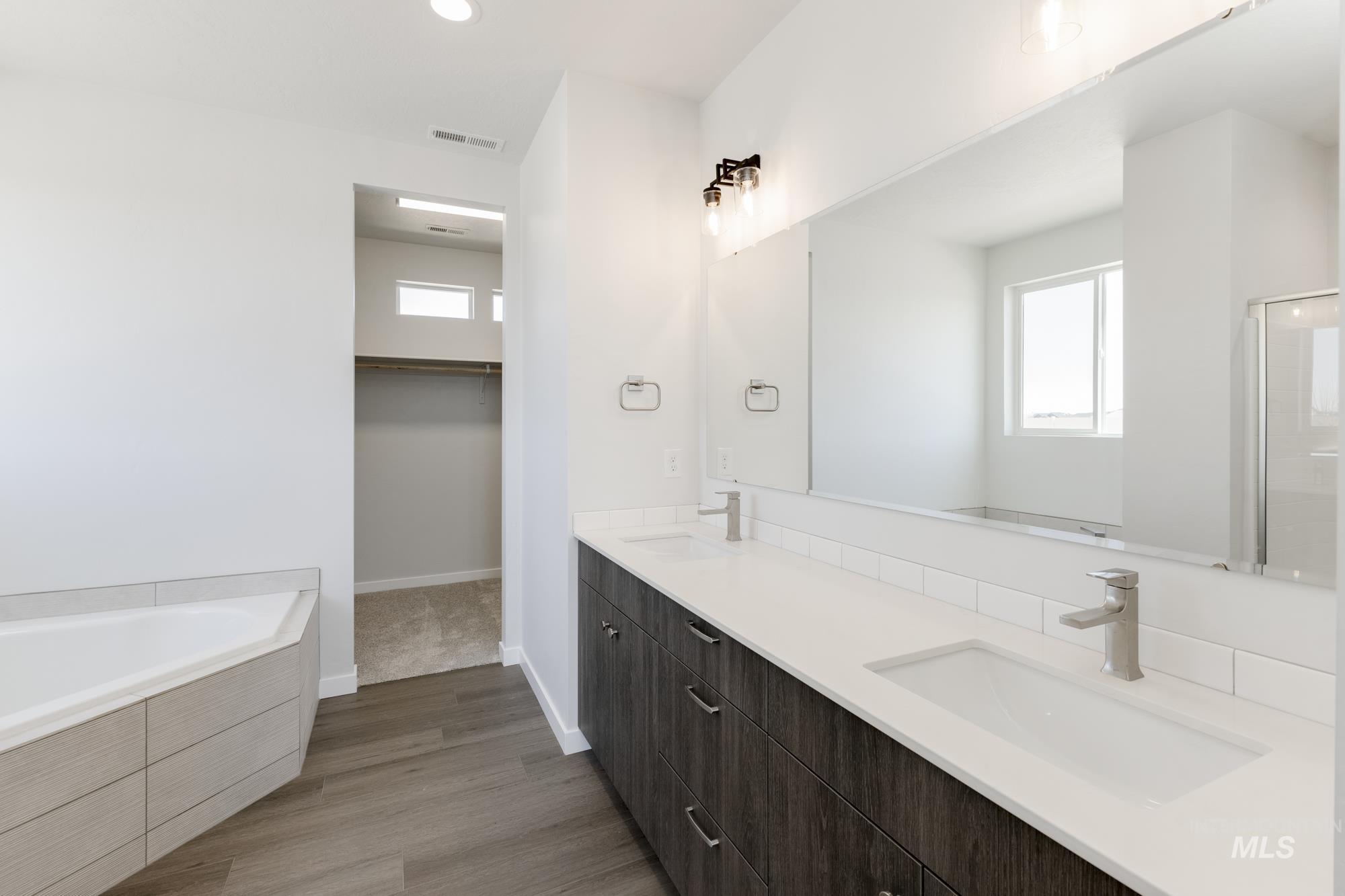 Full bathroom featuring plenty of natural light, double vanity, a bath, dark wood finished floors, and recessed lighting