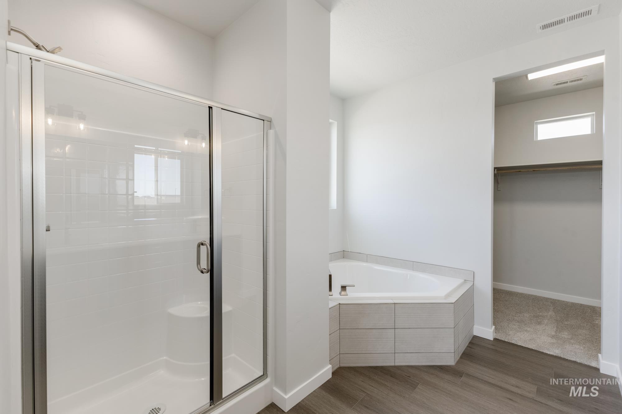 Full bath with a walk in closet, wood finished floors, a stall shower, and a garden tub