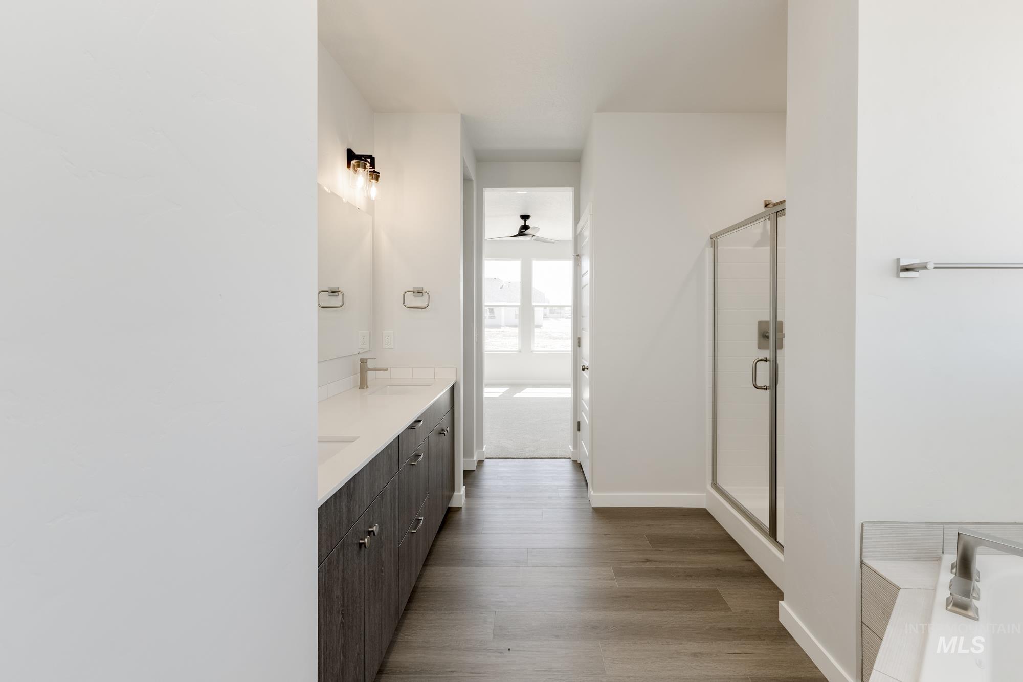 Bathroom with double vanity, dark wood-style floors, a shower stall, and ceiling fan