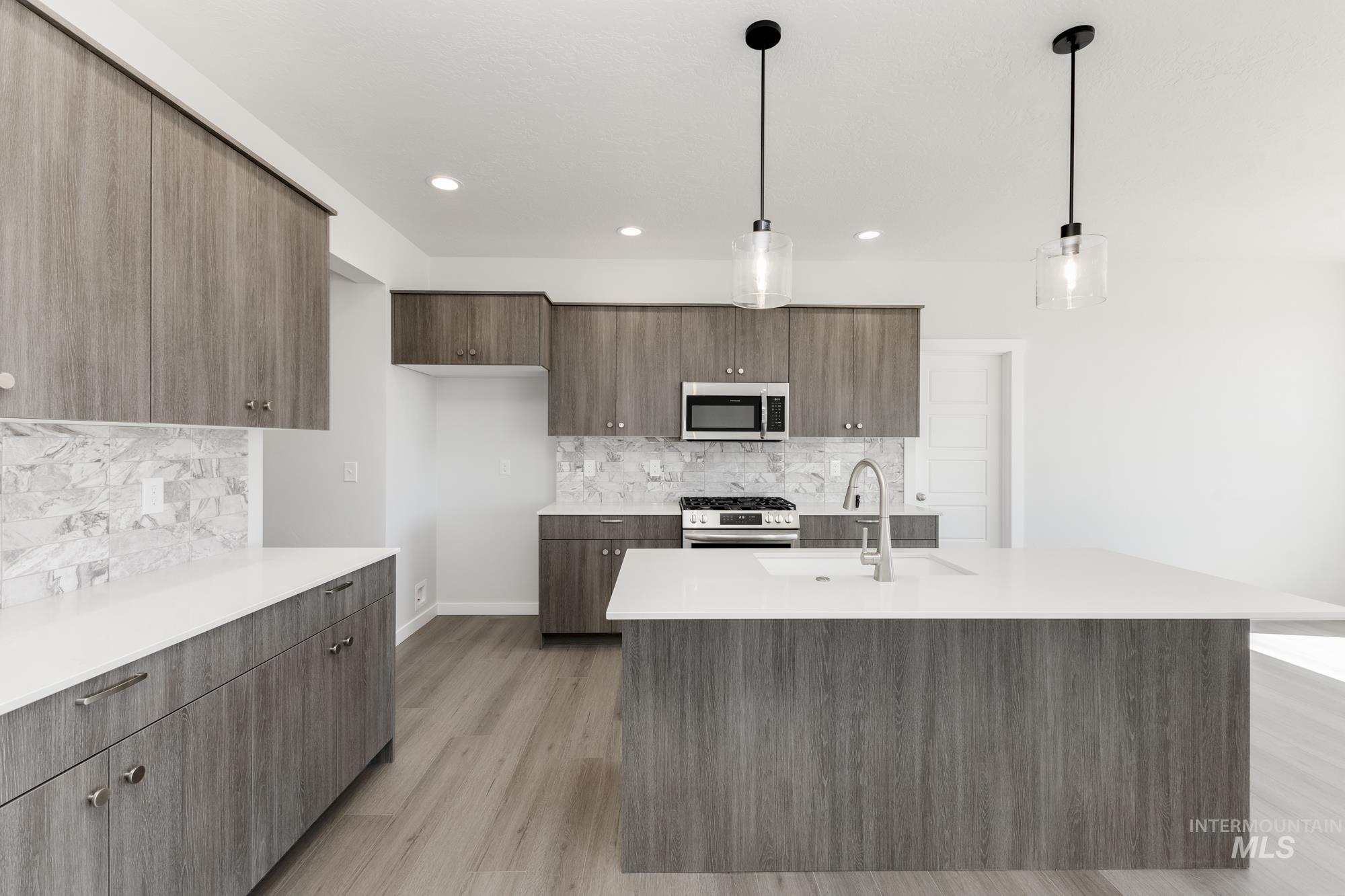 Kitchen featuring pendant lighting, modern cabinets, tasteful backsplash, stainless steel appliances, and light stone countertops