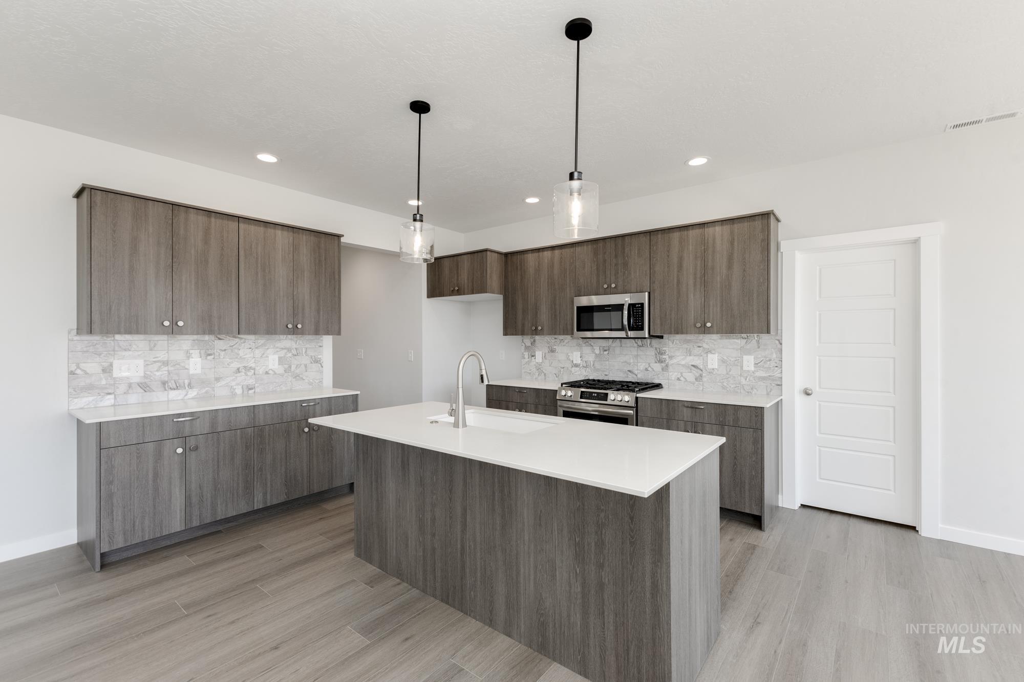 Kitchen with pendant lighting, modern cabinets, stainless steel appliances, an island with sink, and light wood-style floors