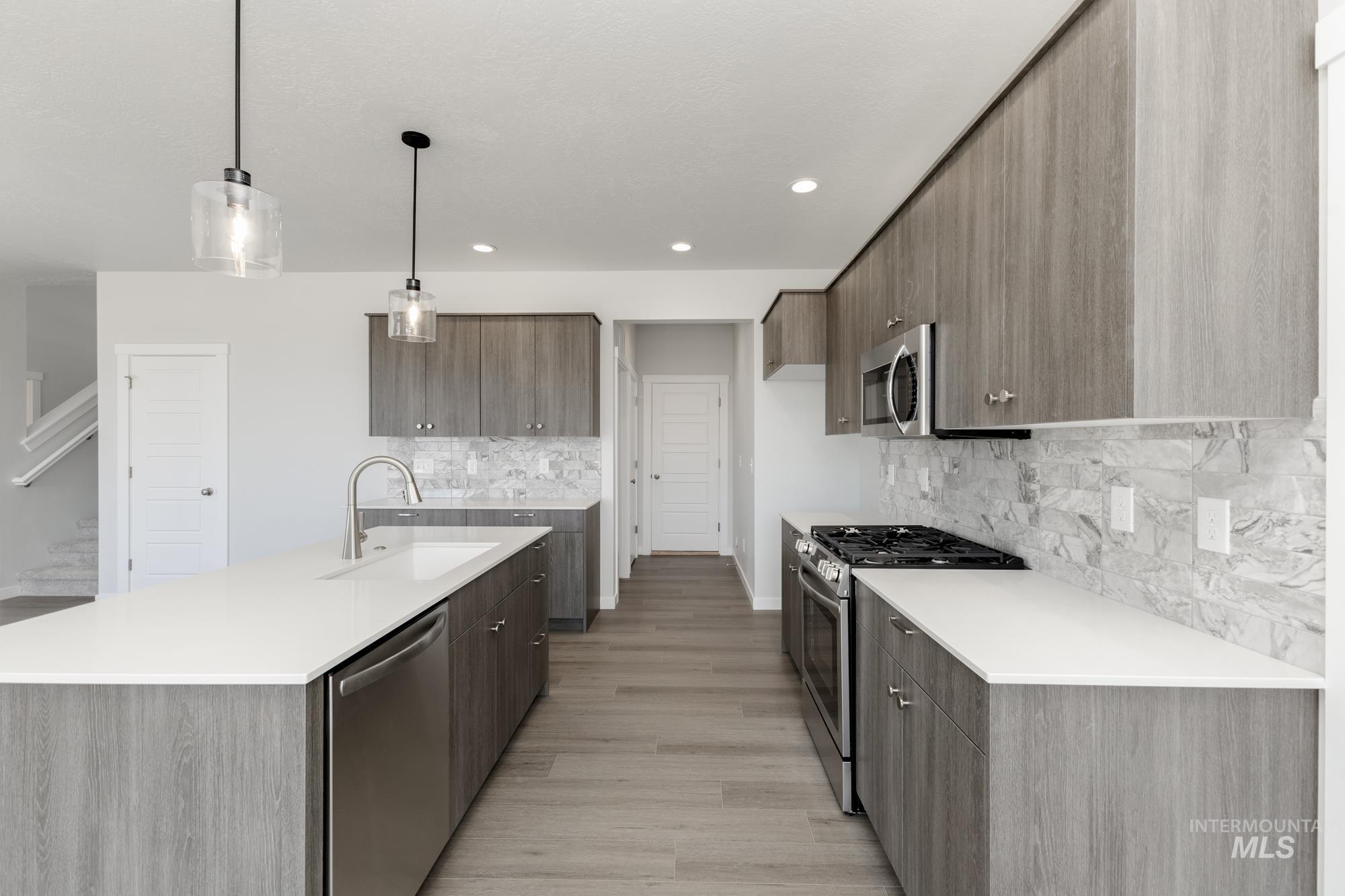Kitchen featuring modern cabinets, stainless steel appliances, decorative light fixtures, an island with sink, and decorative backsplash