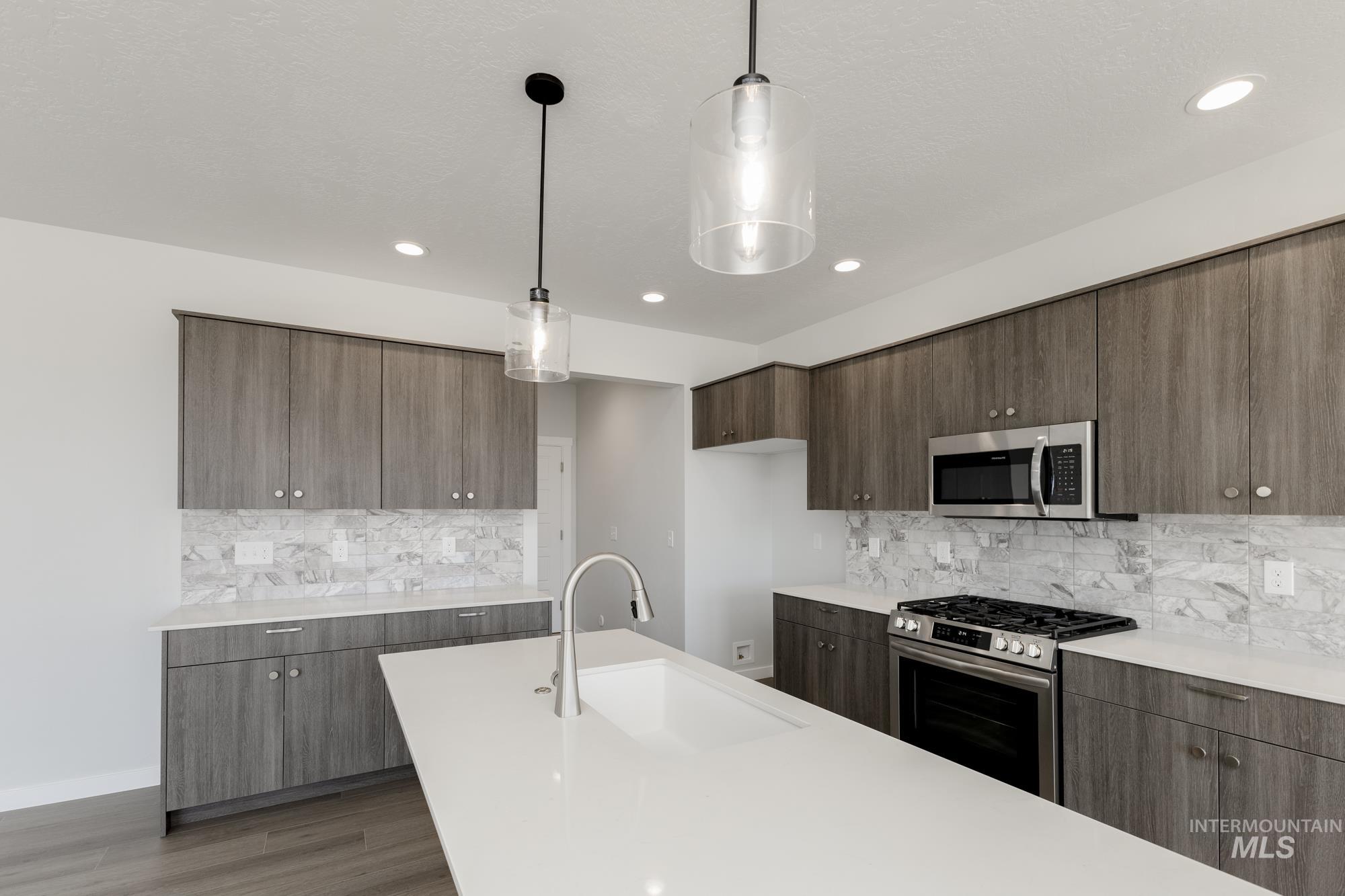 Kitchen with modern cabinets, stainless steel appliances, pendant lighting, light wood-type flooring, and backsplash