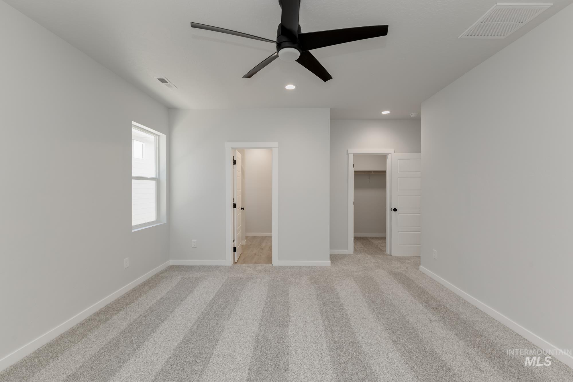 Unfurnished bedroom with light carpet, a spacious closet, recessed lighting, and ceiling fan