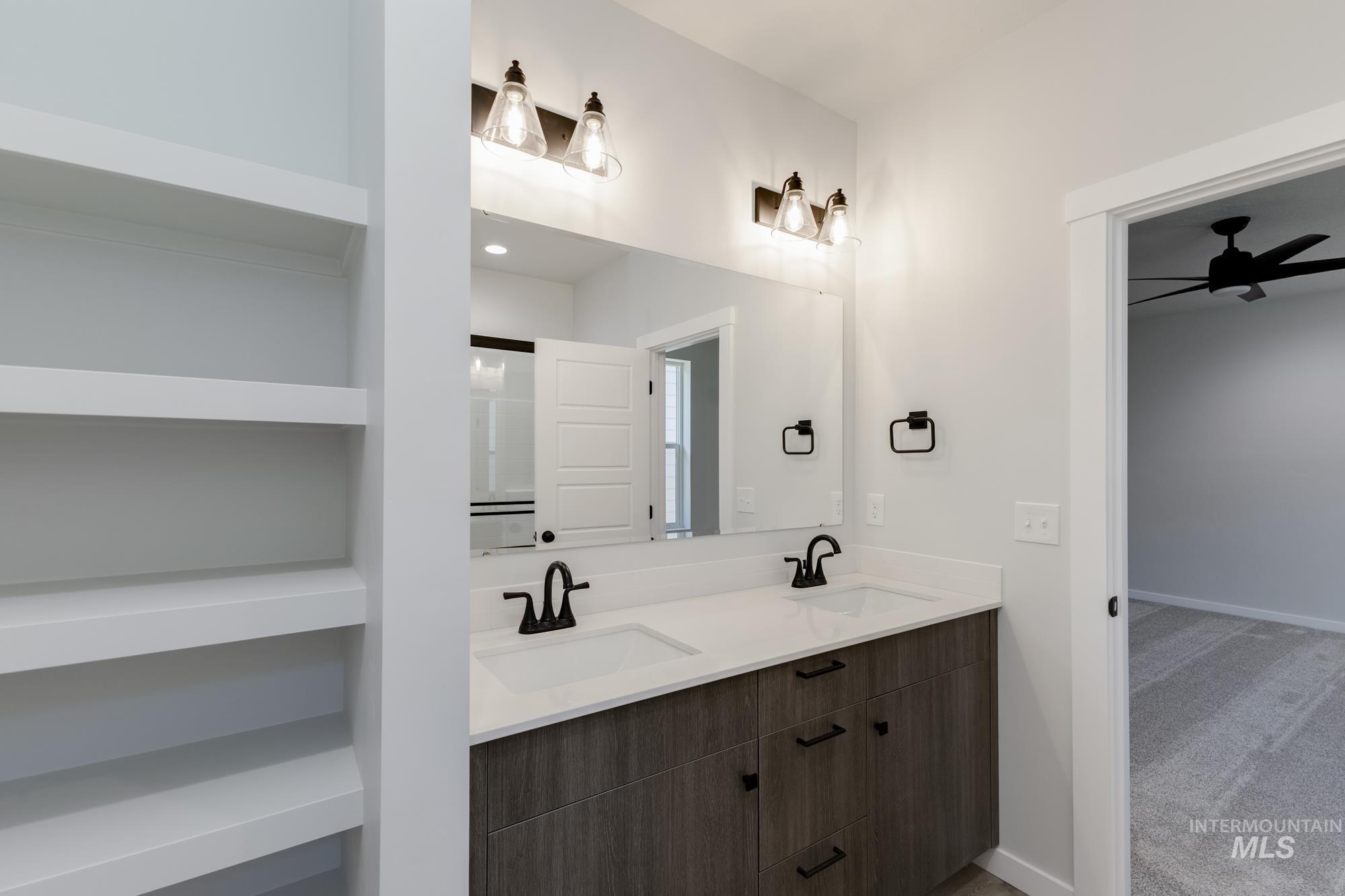 Full bath with double vanity, light carpet, and a ceiling fan