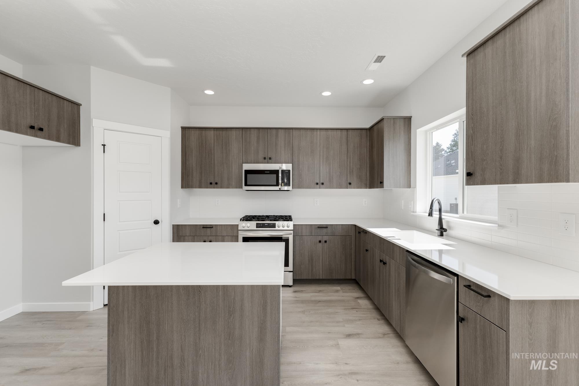 Kitchen with modern cabinets, stainless steel appliances, a kitchen island, light wood finished floors, and recessed lighting