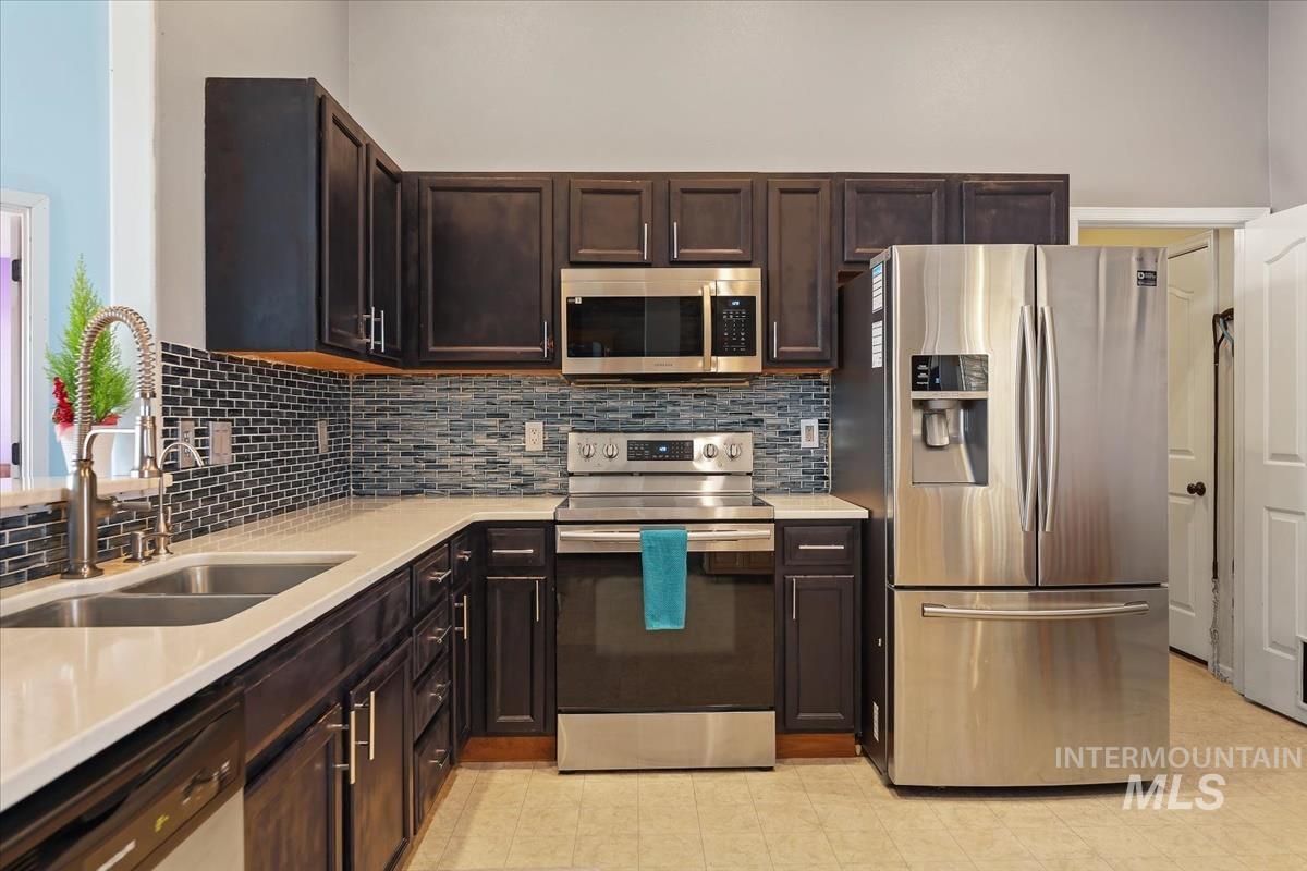 Kitchen with appliances with stainless steel finishes, dark brown cabinets, light stone countertops, and decorative backsplash