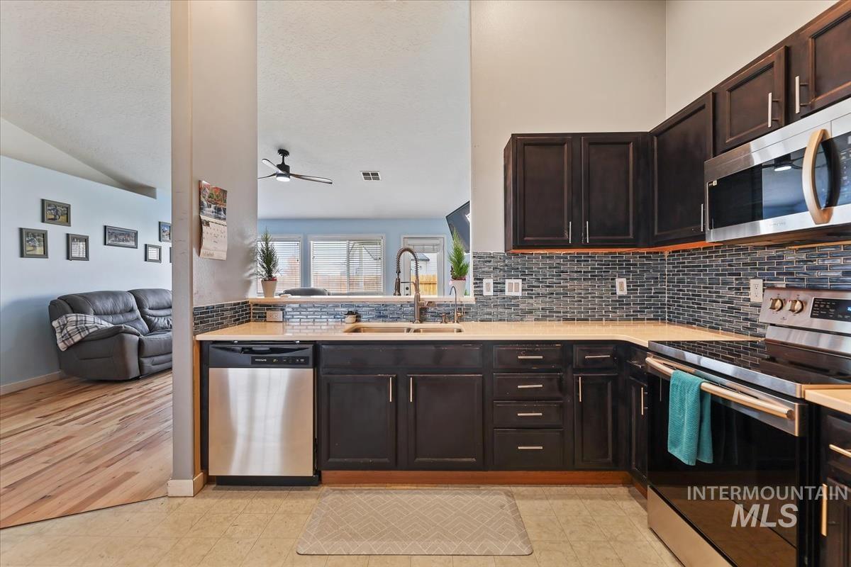 Kitchen with stainless steel appliances, dark brown cabinetry, open floor plan, decorative backsplash, and light floors