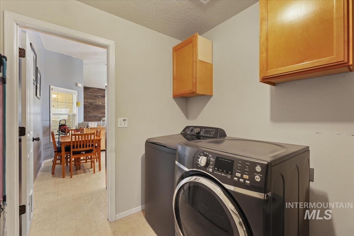 Laundry area with cabinet space, light flooring, washer and clothes dryer, and a textured ceiling