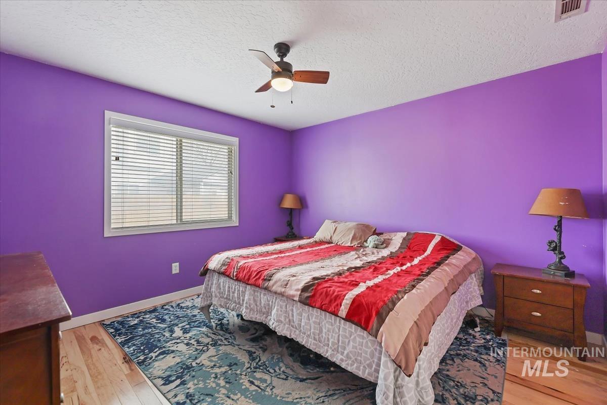 Bedroom with a textured ceiling, ceiling fan, and light wood-type flooring