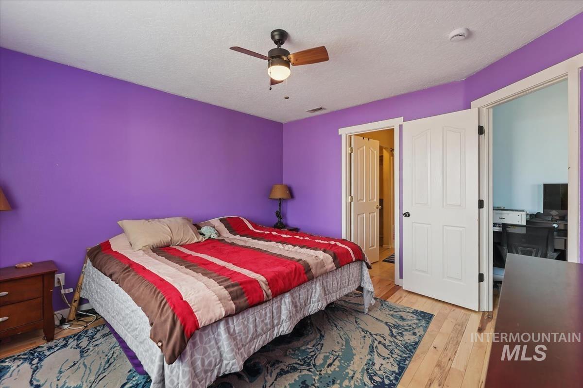 Bedroom with a textured ceiling, light wood finished floors, and a ceiling fan