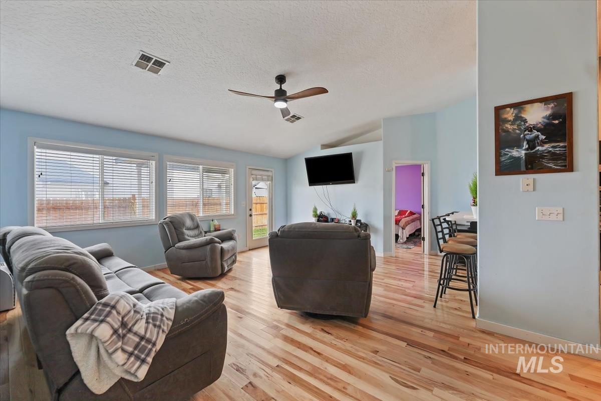Living area featuring ceiling fan, lofted ceiling, light wood finished floors, and a textured ceiling