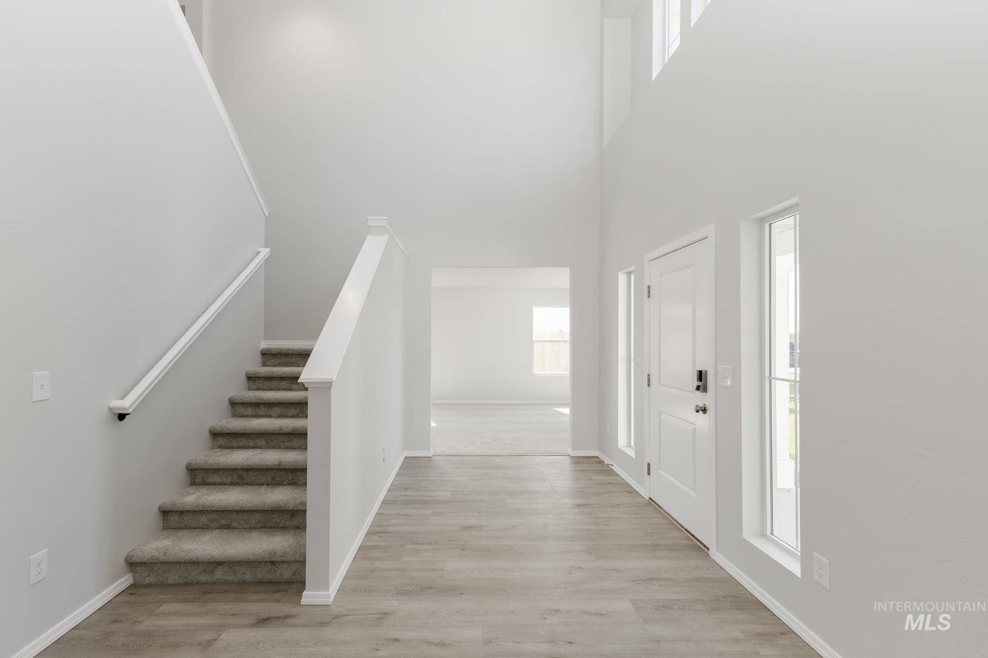 Foyer entrance with stairway, light wood finished floors, and a high ceiling