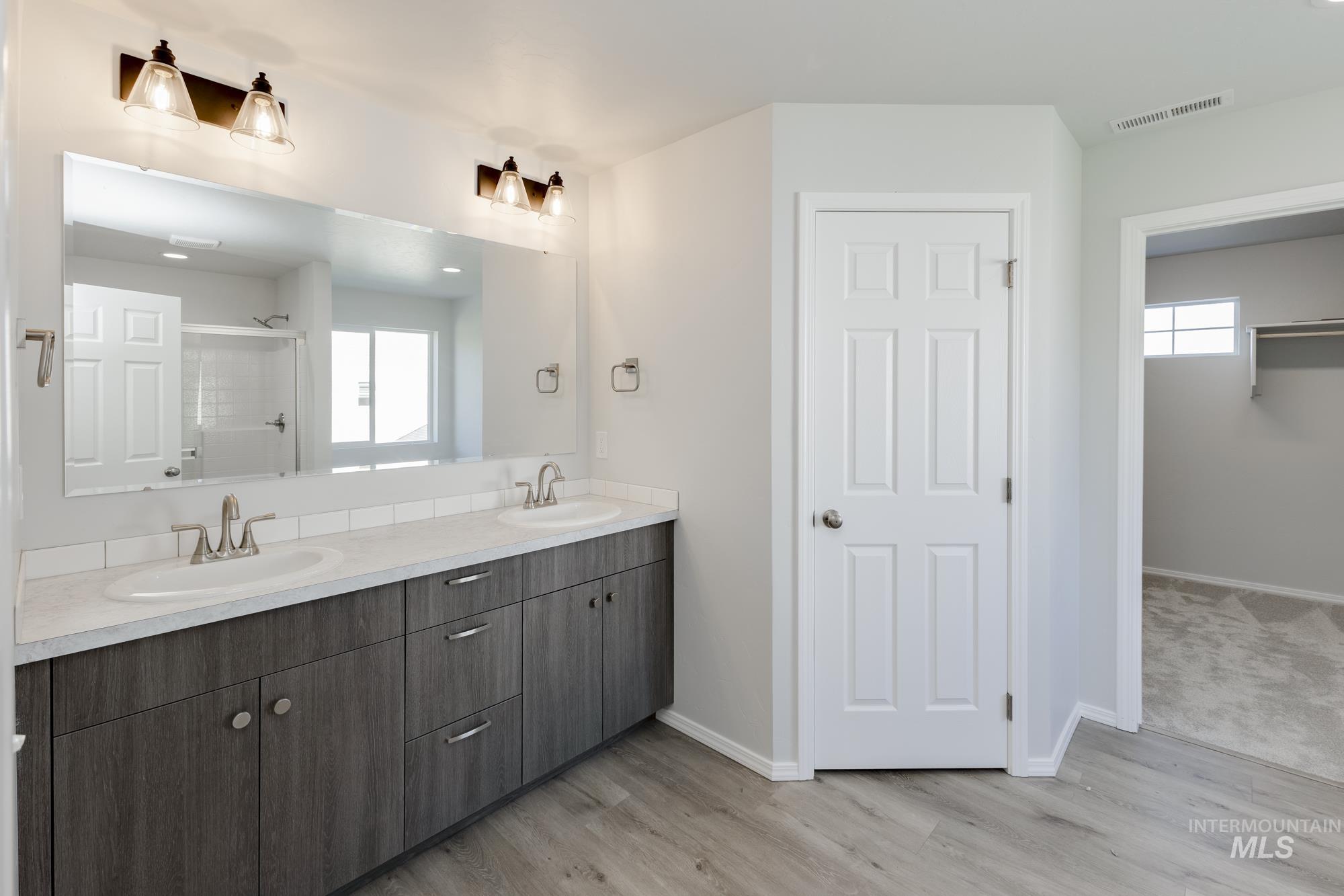 Bathroom featuring double vanity, a walk in shower, a spacious closet, and light wood finished floors