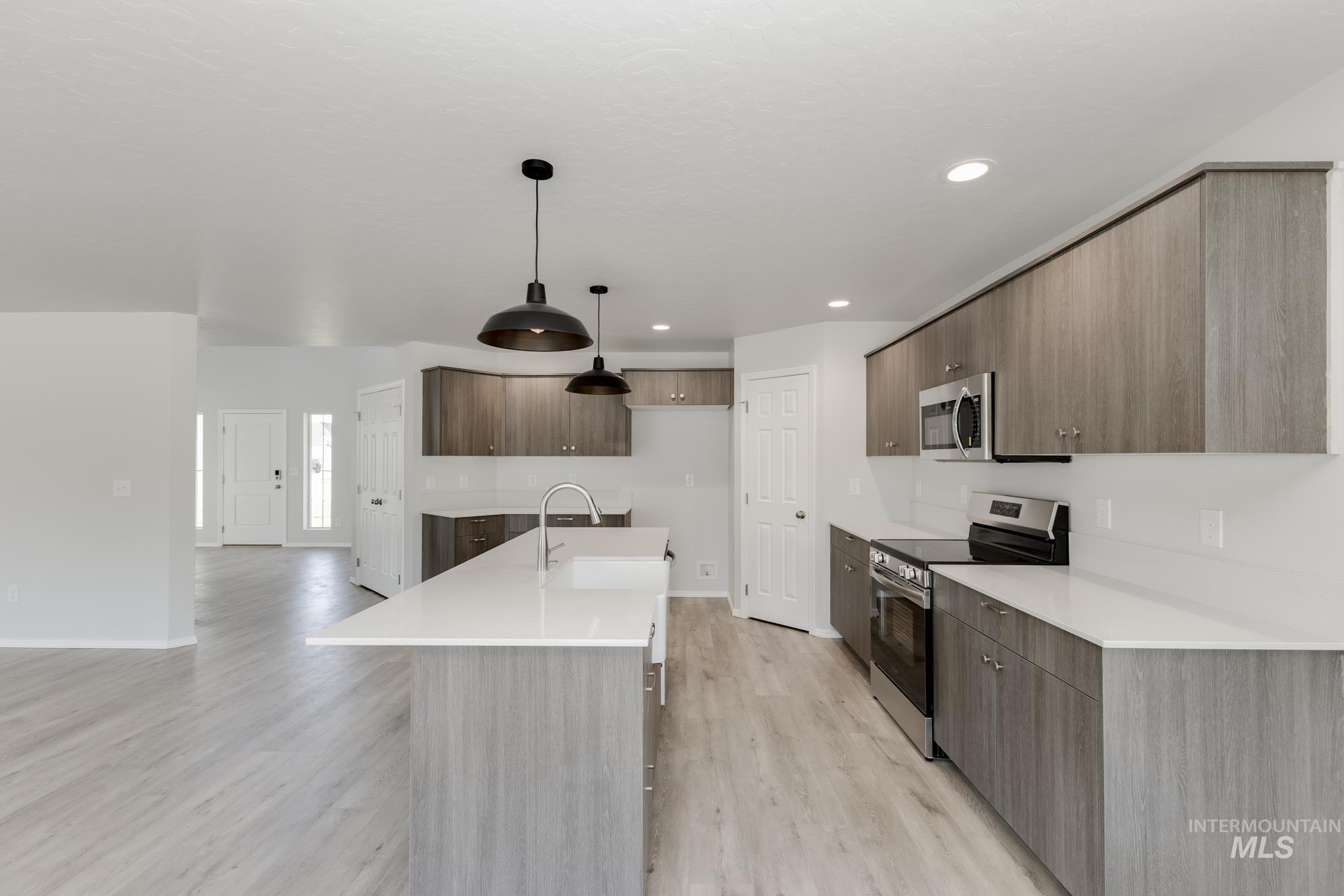 Kitchen with appliances with stainless steel finishes, modern cabinets, hanging light fixtures, an island with sink, and light wood-style floors