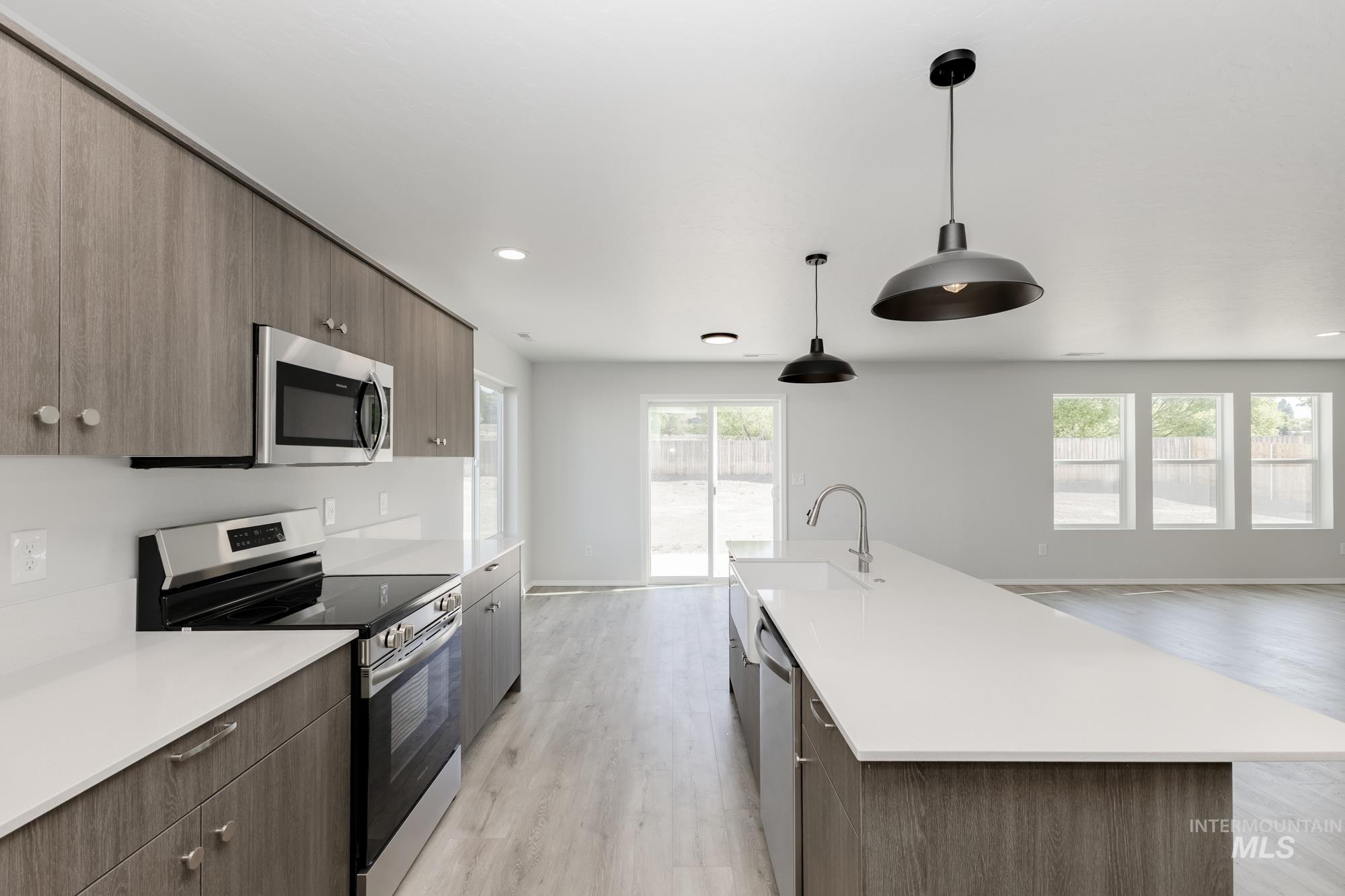Kitchen featuring appliances with stainless steel finishes, light wood-style flooring, decorative light fixtures, modern cabinets, and a kitchen island with sink