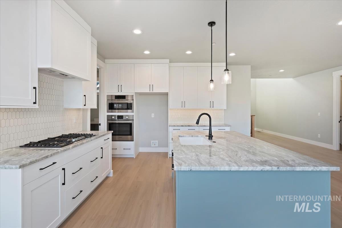 Kitchen featuring white cabinets, pendant lighting, a kitchen island with sink, light stone countertops, and light wood finished floors