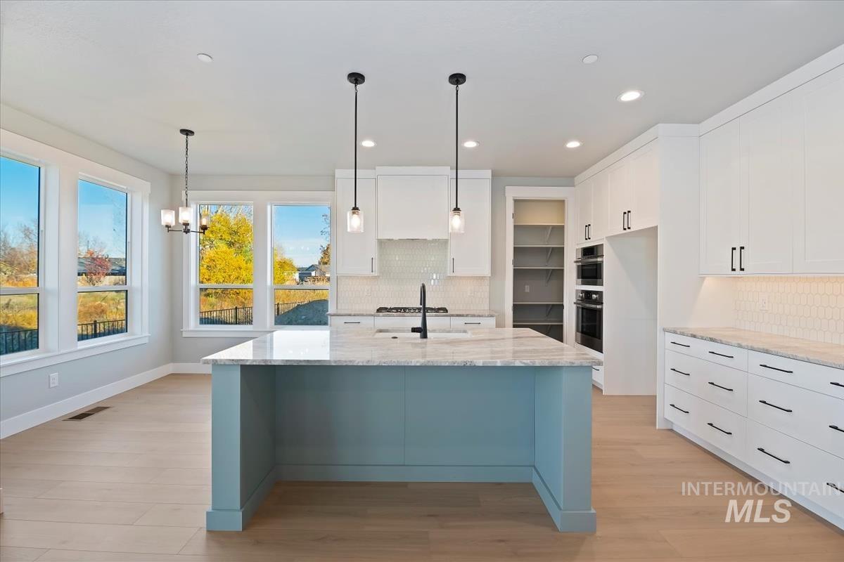 Kitchen with light stone countertops, white cabinetry, recessed lighting, pendant lighting, and light wood finished floors
