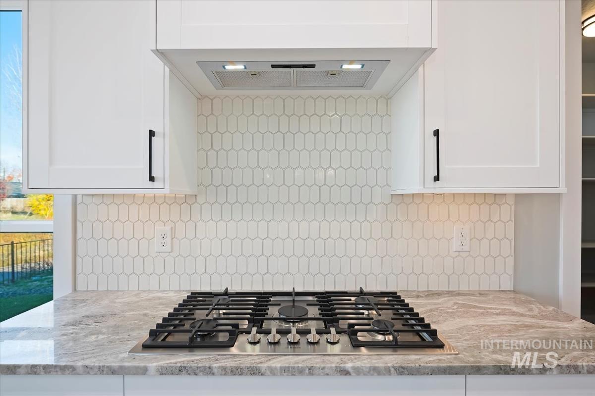 Kitchen featuring under cabinet range hood, stainless steel gas stovetop, light stone countertops, and white cabinetry