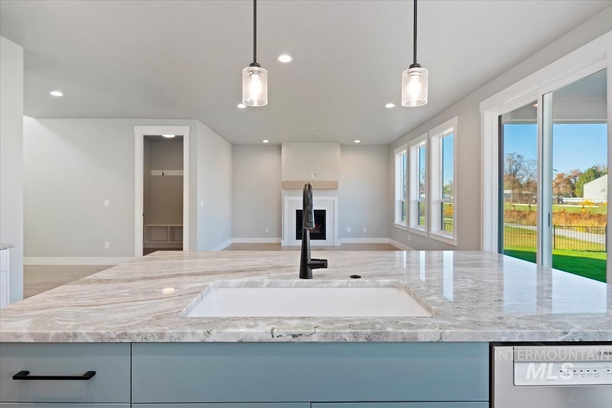 Kitchen with light stone counters, hanging light fixtures, dishwasher, a fireplace, and recessed lighting