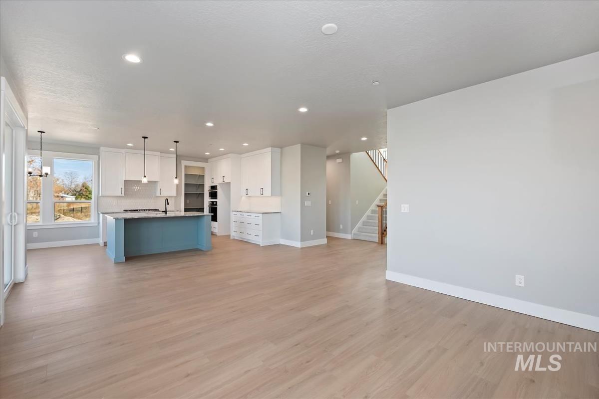 Unfurnished living room featuring stairs, recessed lighting, light wood-style flooring, and a chandelier