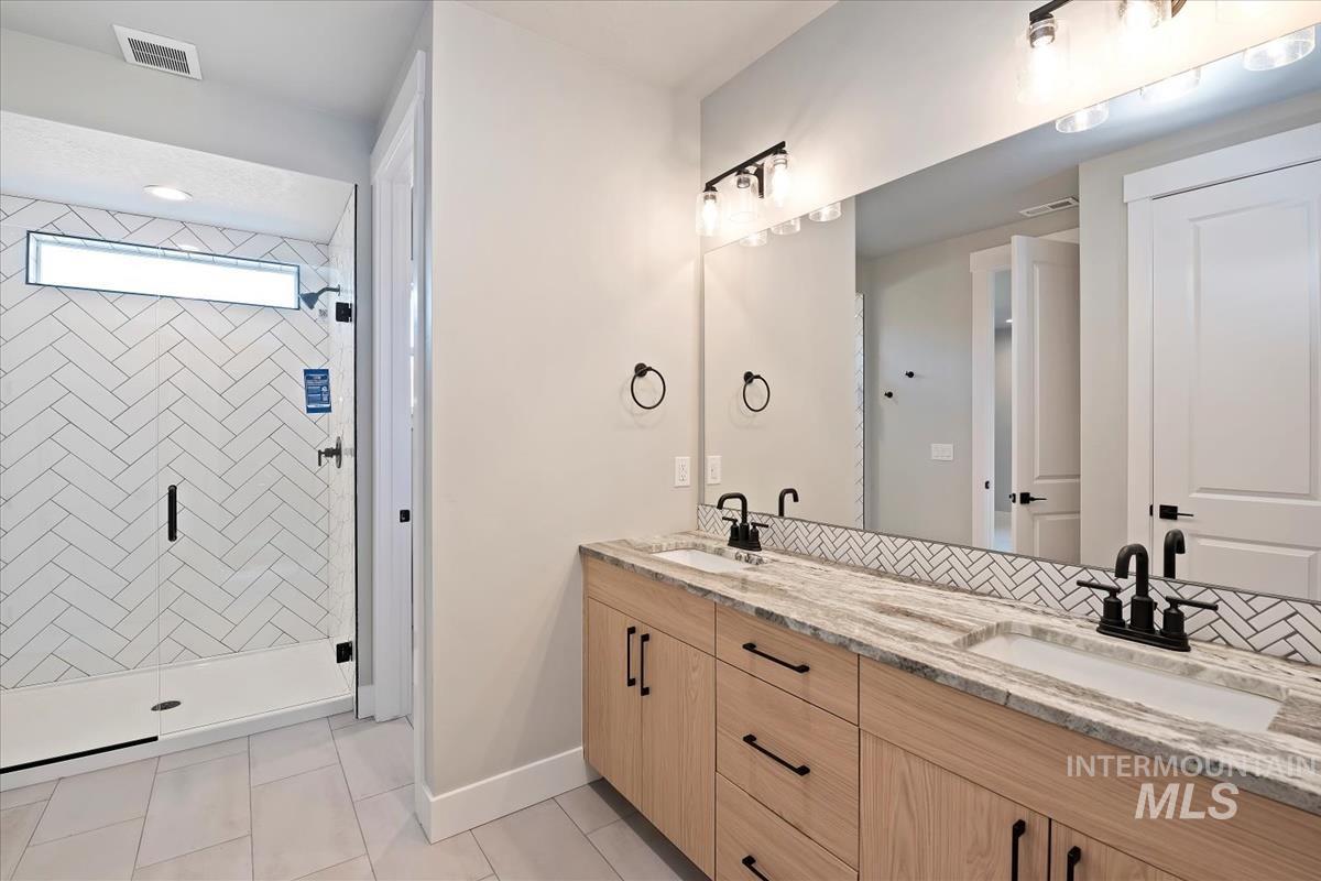 Bathroom featuring double vanity, a shower stall, and light tile patterned floors
