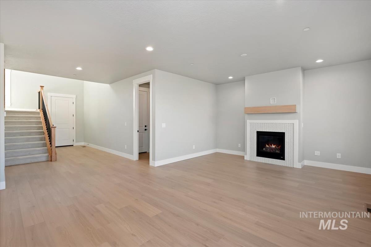 Unfurnished living room with recessed lighting, light wood-style floors, stairs, and a tile fireplace