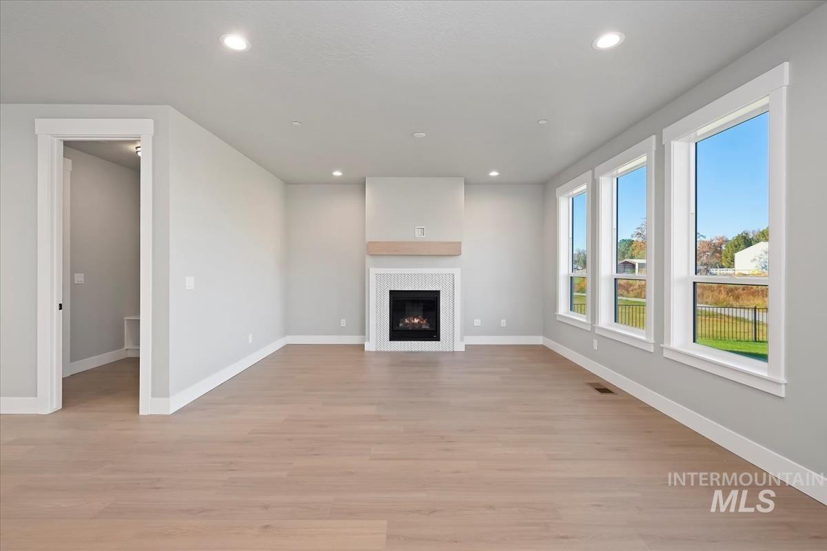 Unfurnished living room featuring light wood-type flooring, recessed lighting, and a warm lit fireplace