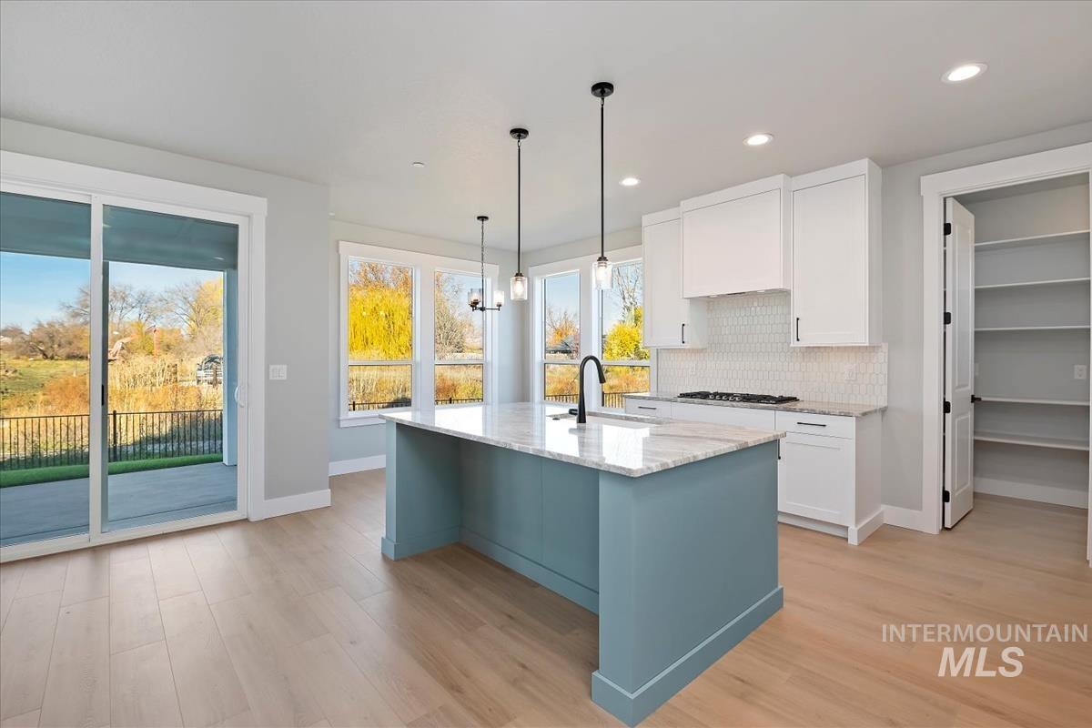 Kitchen with white cabinets, tasteful backsplash, decorative light fixtures, light stone countertops, and light wood-style flooring
