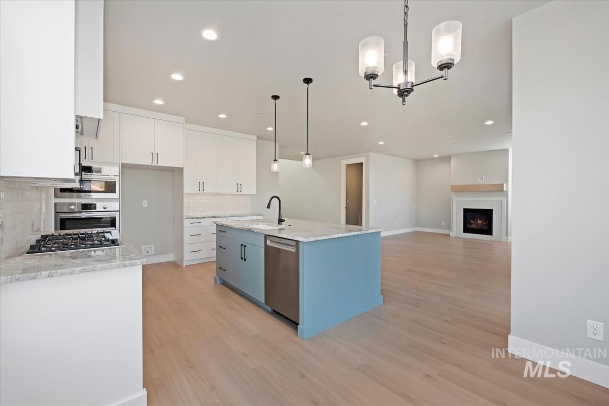 Kitchen featuring hanging light fixtures, a warm lit fireplace, white cabinets, a chandelier, and light stone counters