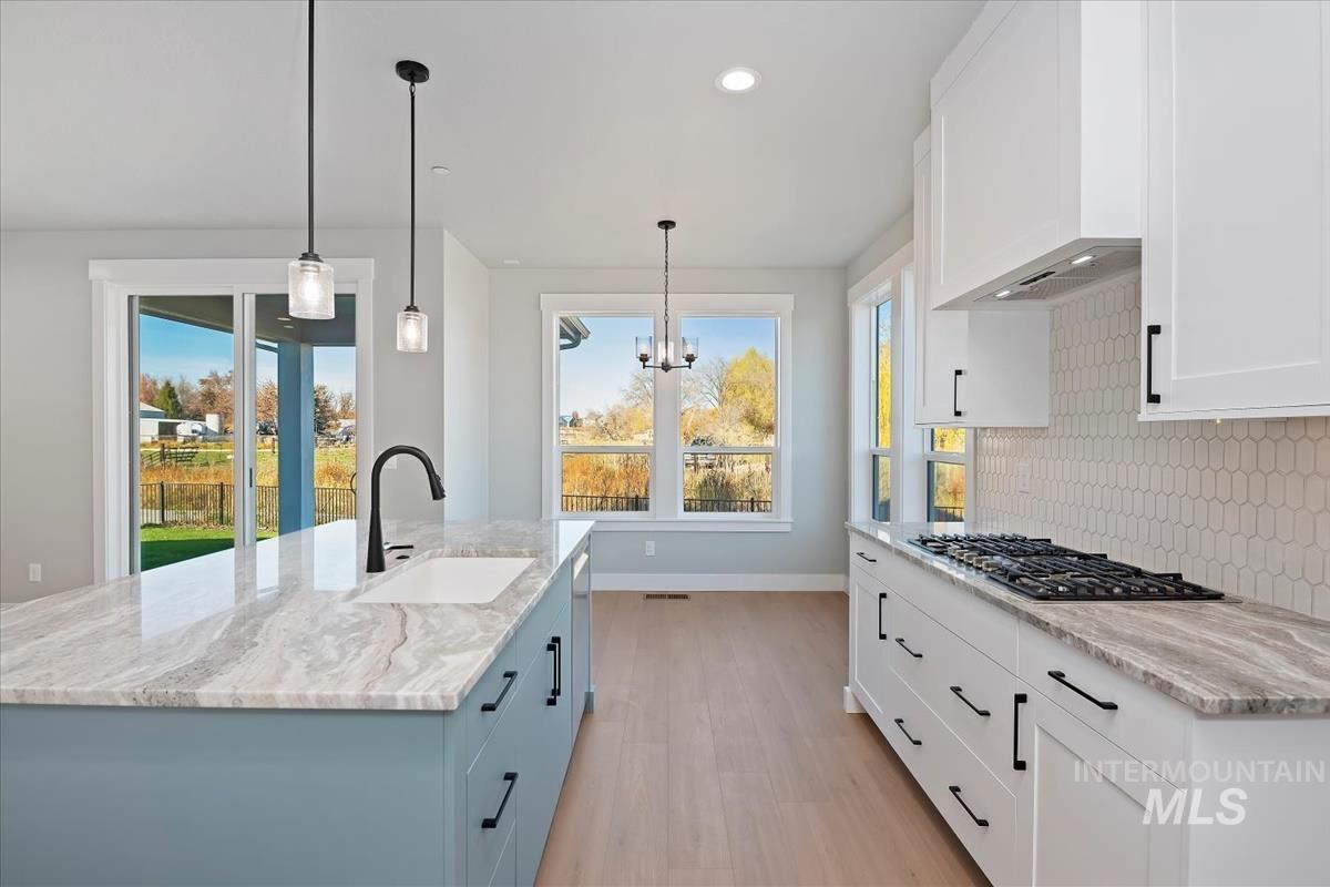 Kitchen featuring white cabinetry, decorative light fixtures, light stone counters, recessed lighting, and a kitchen island with sink