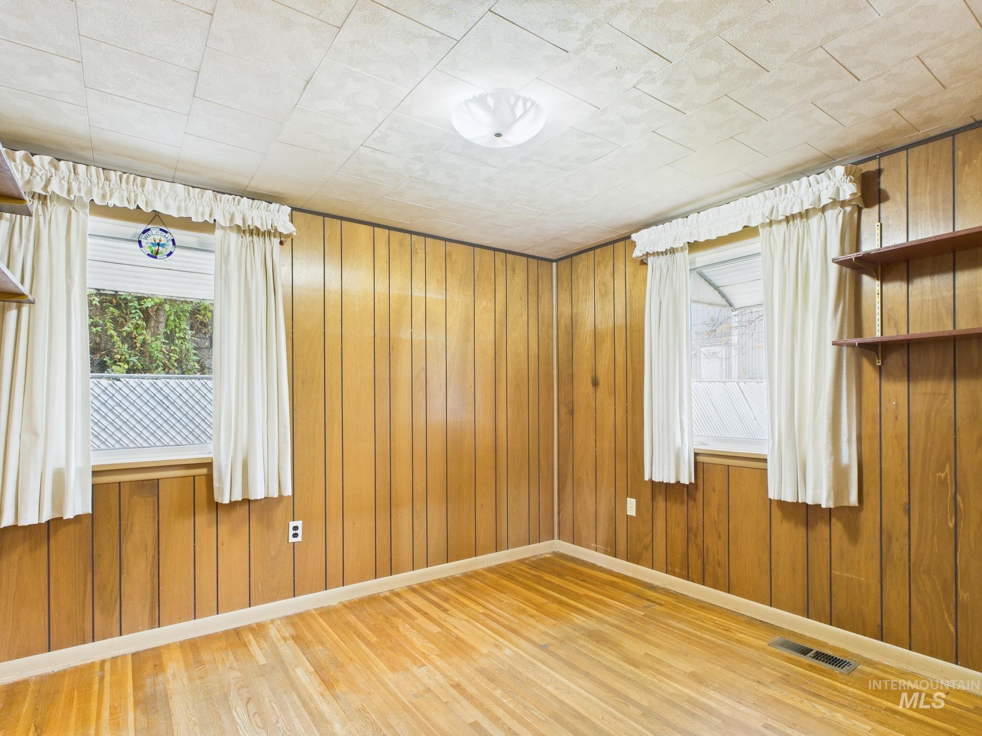 Unfurnished room with light wood-style flooring, wood walls, and healthy amount of natural light