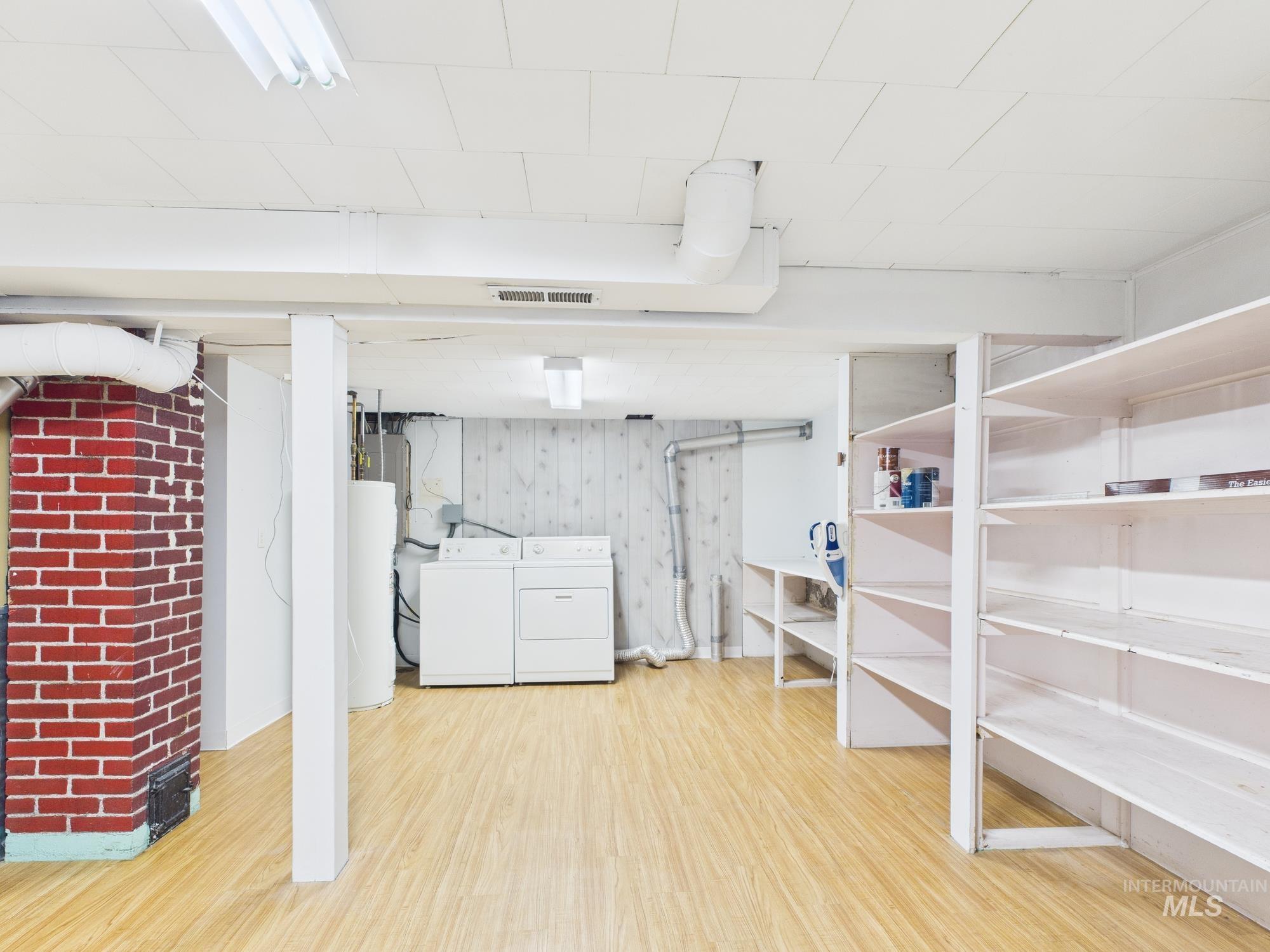 Finished basement with light wood-style floors, washer and dryer, water heater, and wood walls