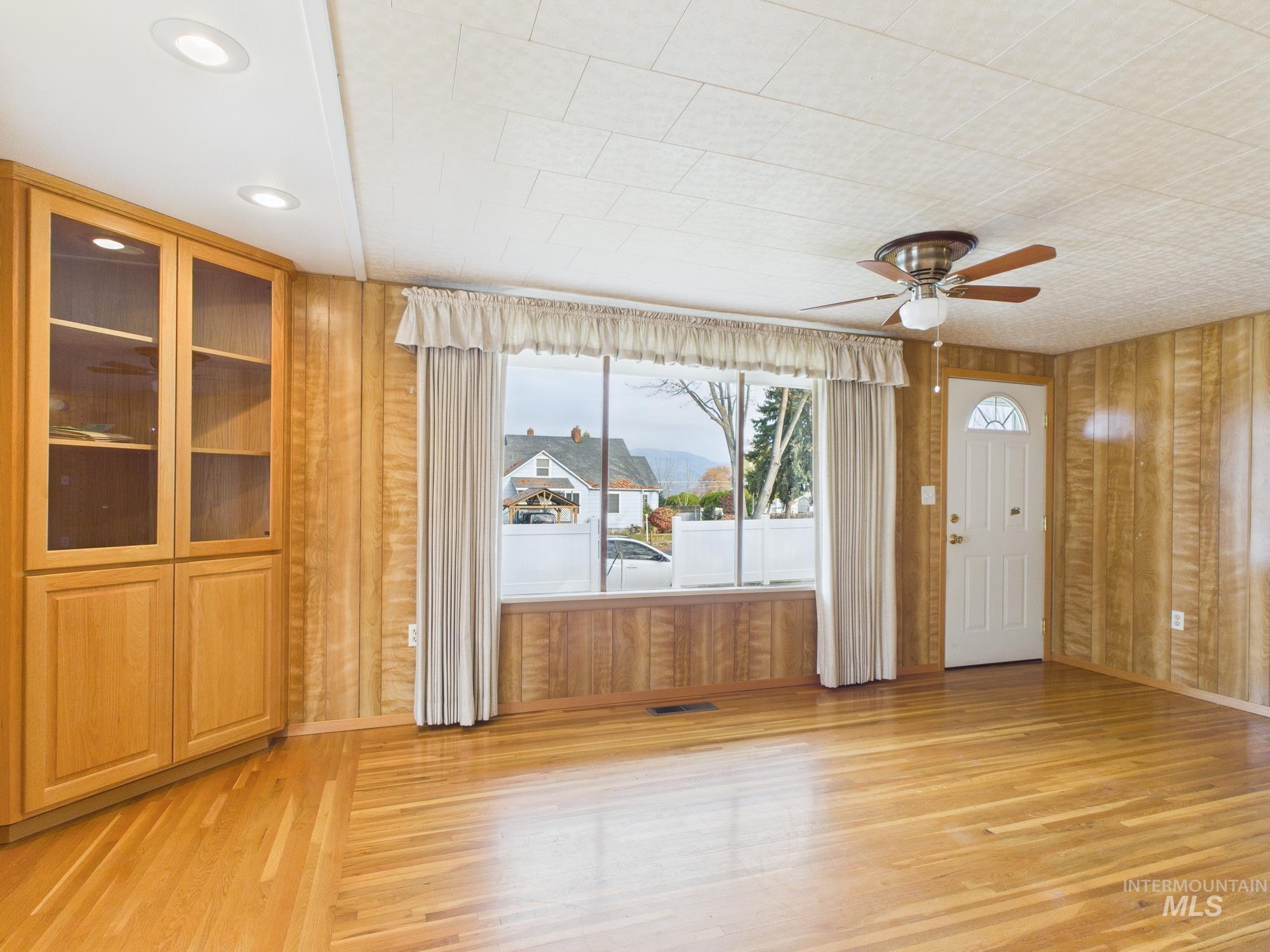 Spare room with wooden walls, light wood-style floors, and a ceiling fan