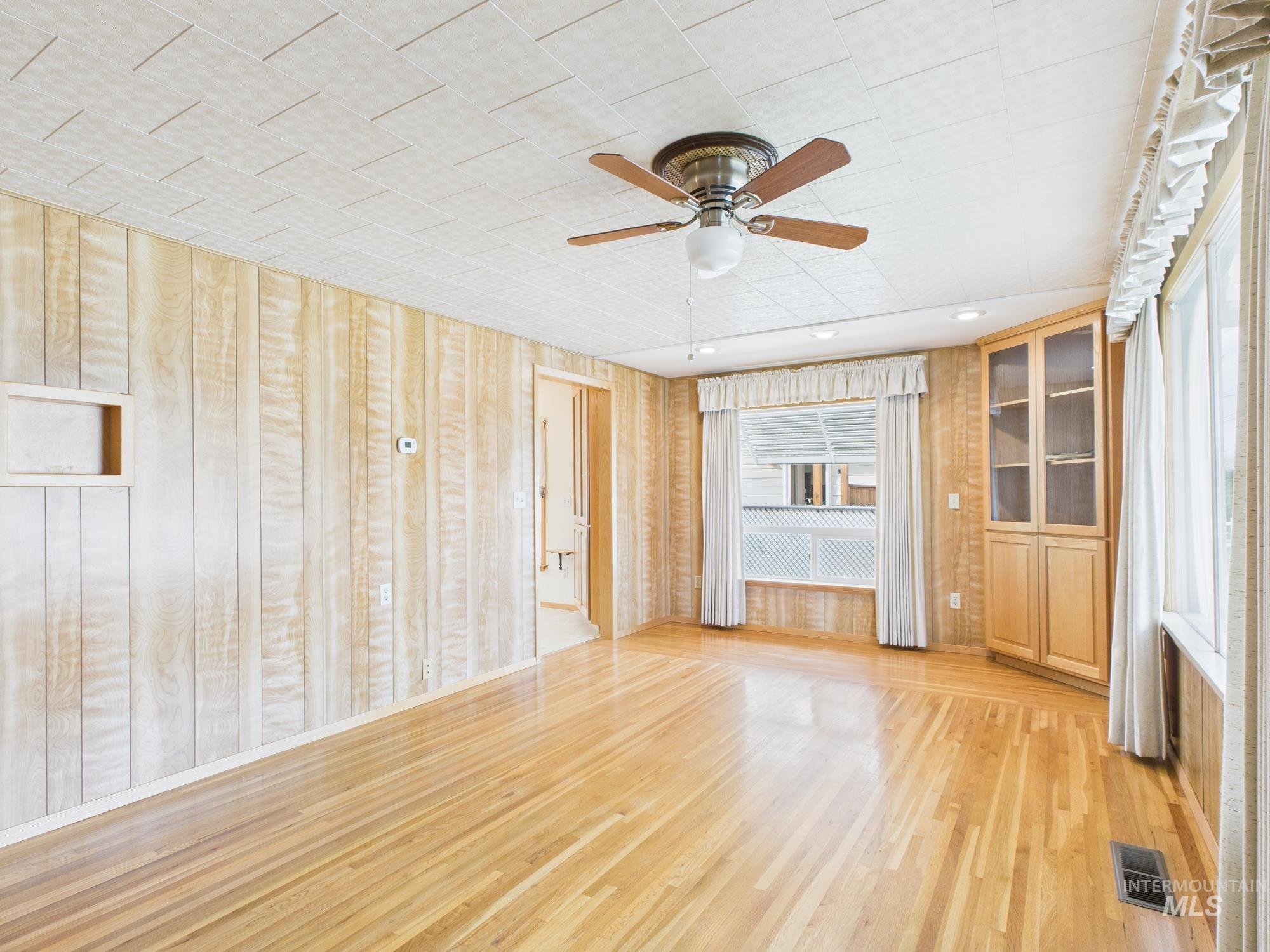Unfurnished living room featuring light wood-style floors, a ceiling fan, and wooden walls