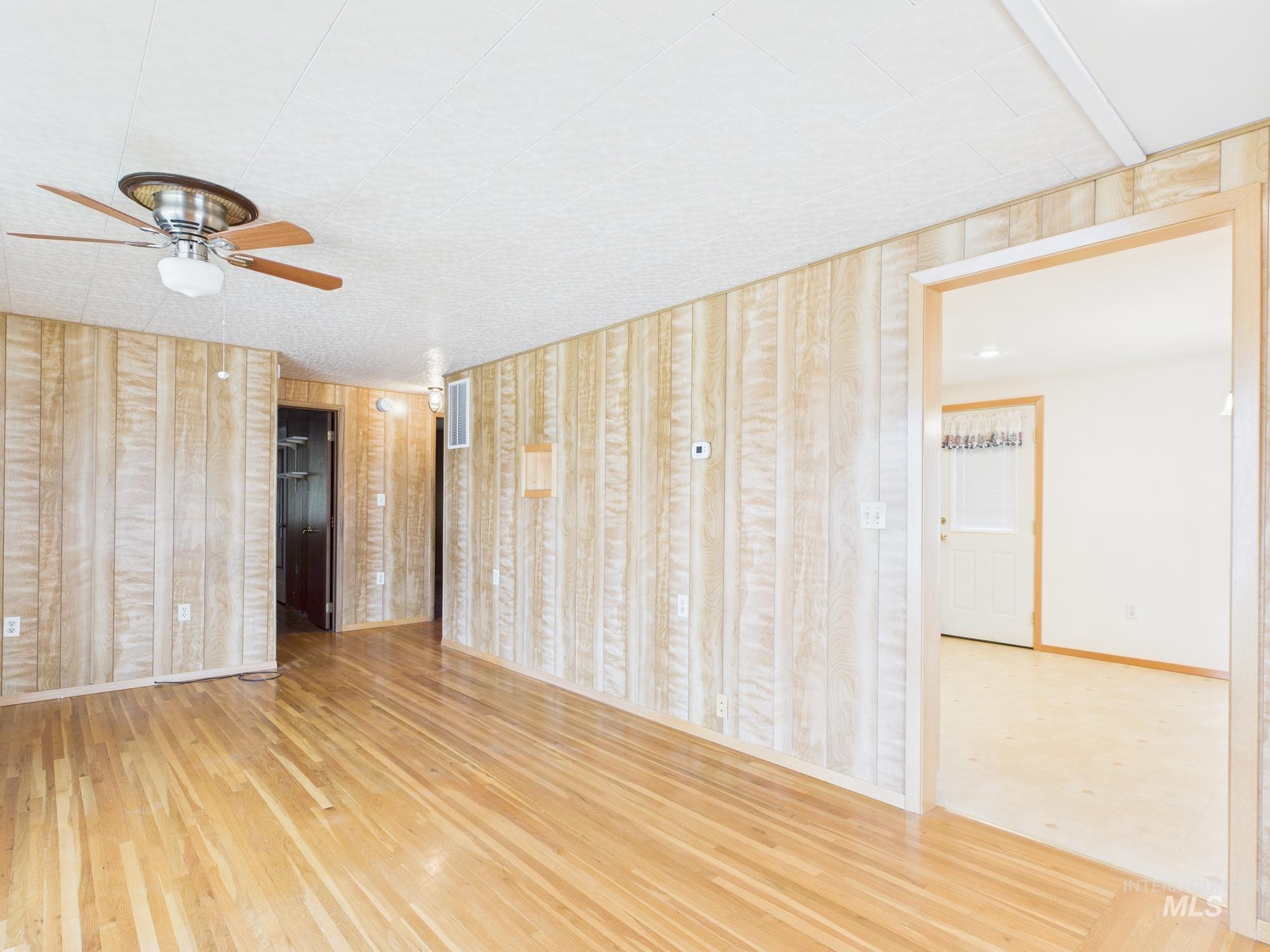 Spare room with light wood finished floors, a ceiling fan, and wood walls
