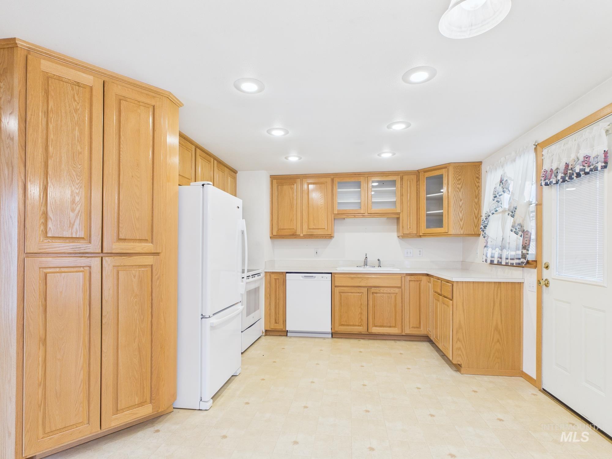 Kitchen with light floors, white appliances, glass insert cabinets, light countertops, and recessed lighting