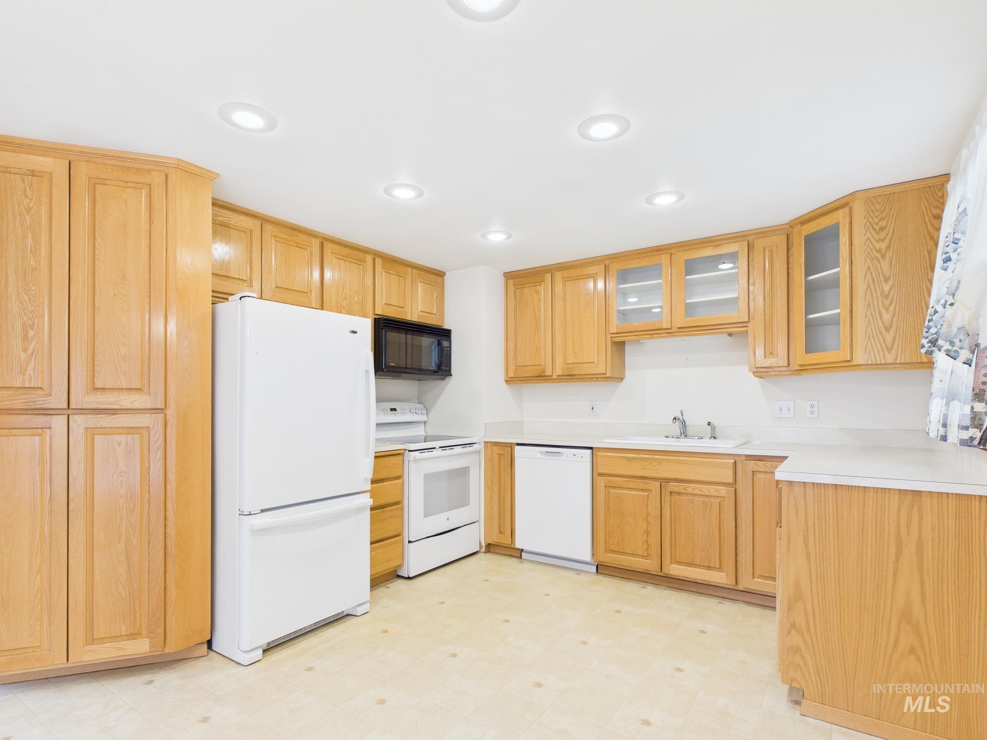 Kitchen featuring light floors, light countertops, white appliances, glass insert cabinets, and recessed lighting
