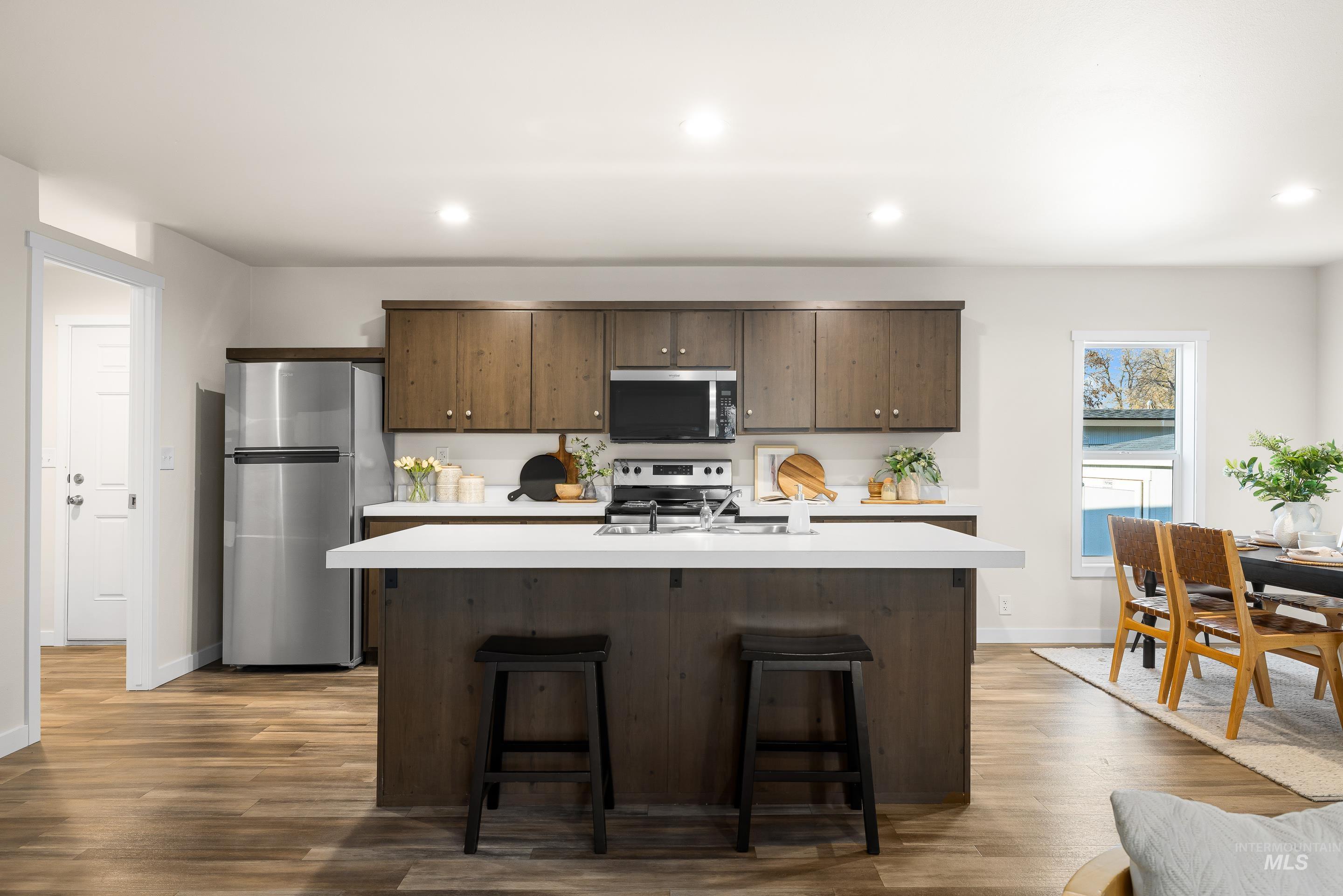 Kitchen with dark brown cabinets, stainless steel appliances, light countertops, a breakfast bar area, and recessed lighting