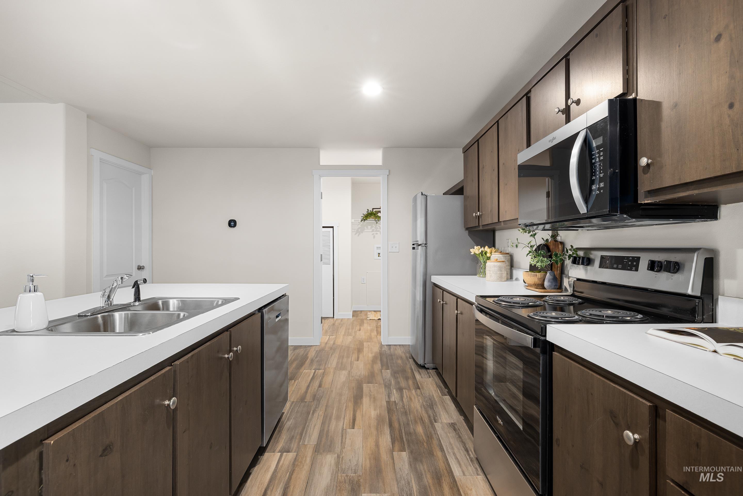 Kitchen with dark brown cabinets, appliances with stainless steel finishes, light countertops, light wood-type flooring, and recessed lighting