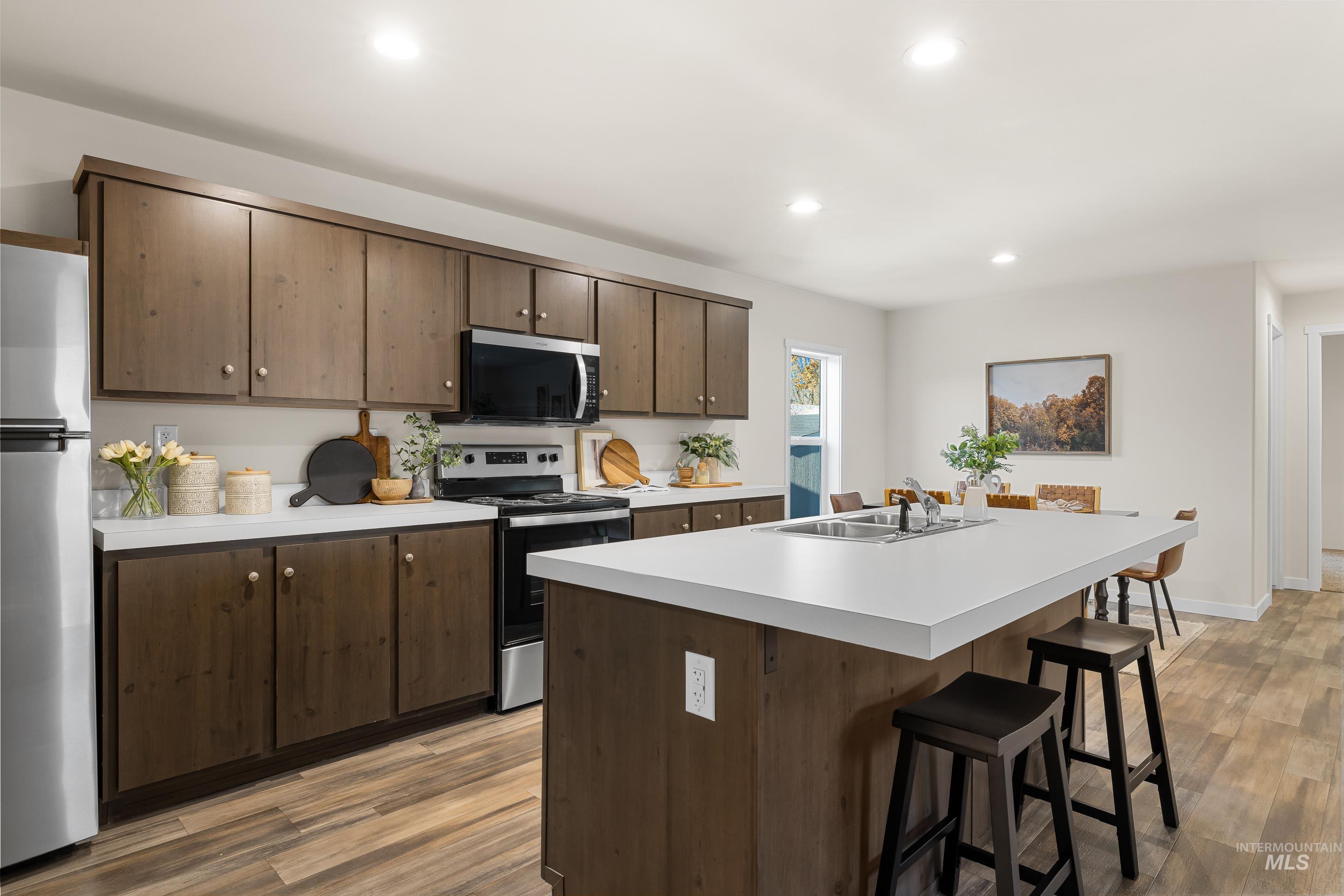 Kitchen with light countertops, appliances with stainless steel finishes, recessed lighting, light wood finished floors, and an island with sink