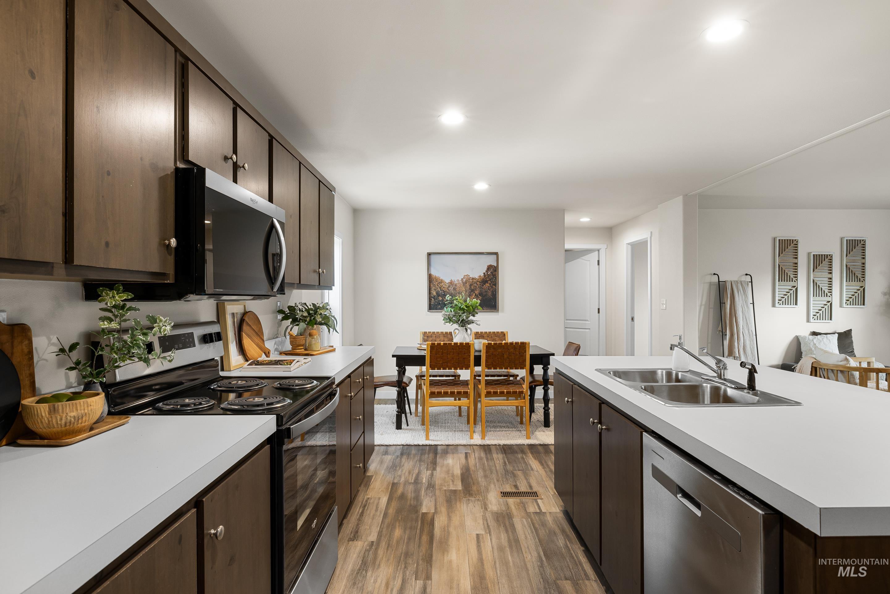 Kitchen with dark brown cabinets, appliances with stainless steel finishes, light countertops, dark wood-style floors, and recessed lighting